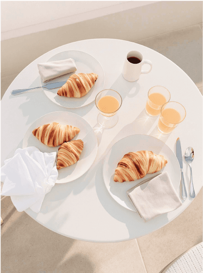 Minimalist breakfast setup with croissants, orange juice, and coffee on a white table.