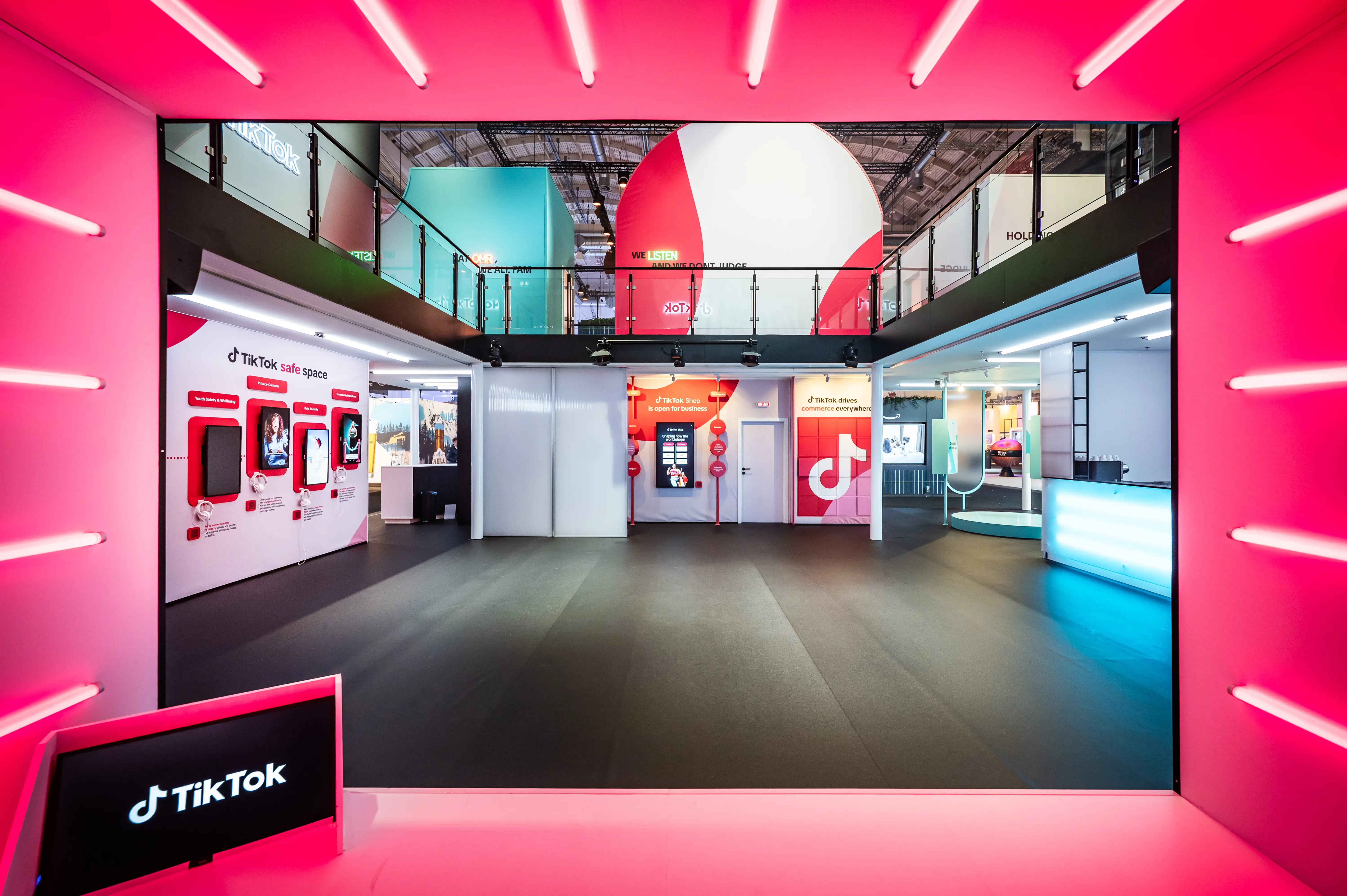 View through a pink neon-lit frame into the open booth interior with TikTok safe space wall and reception.
