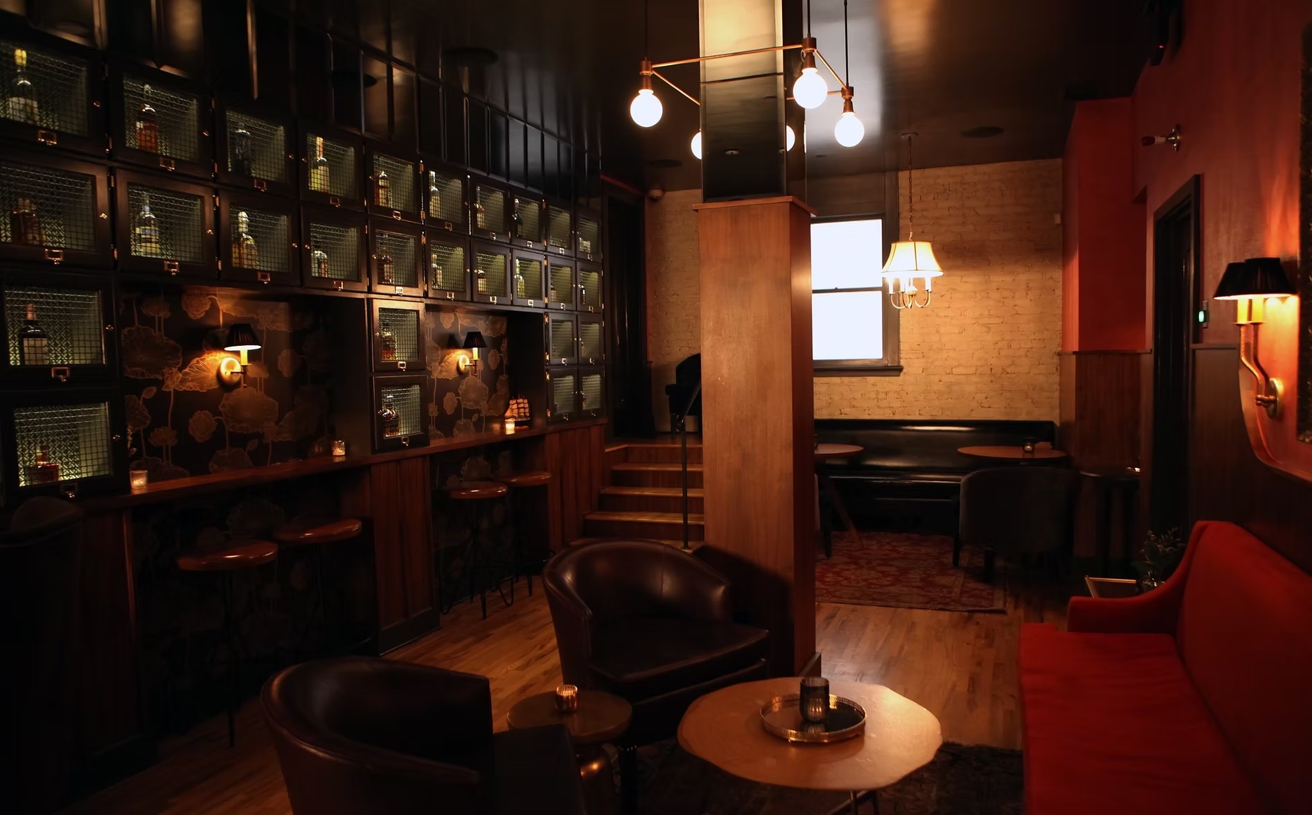 Walker Inn interior with dark liquor cabinets, brass globe lights, leather seating and a red banquette.