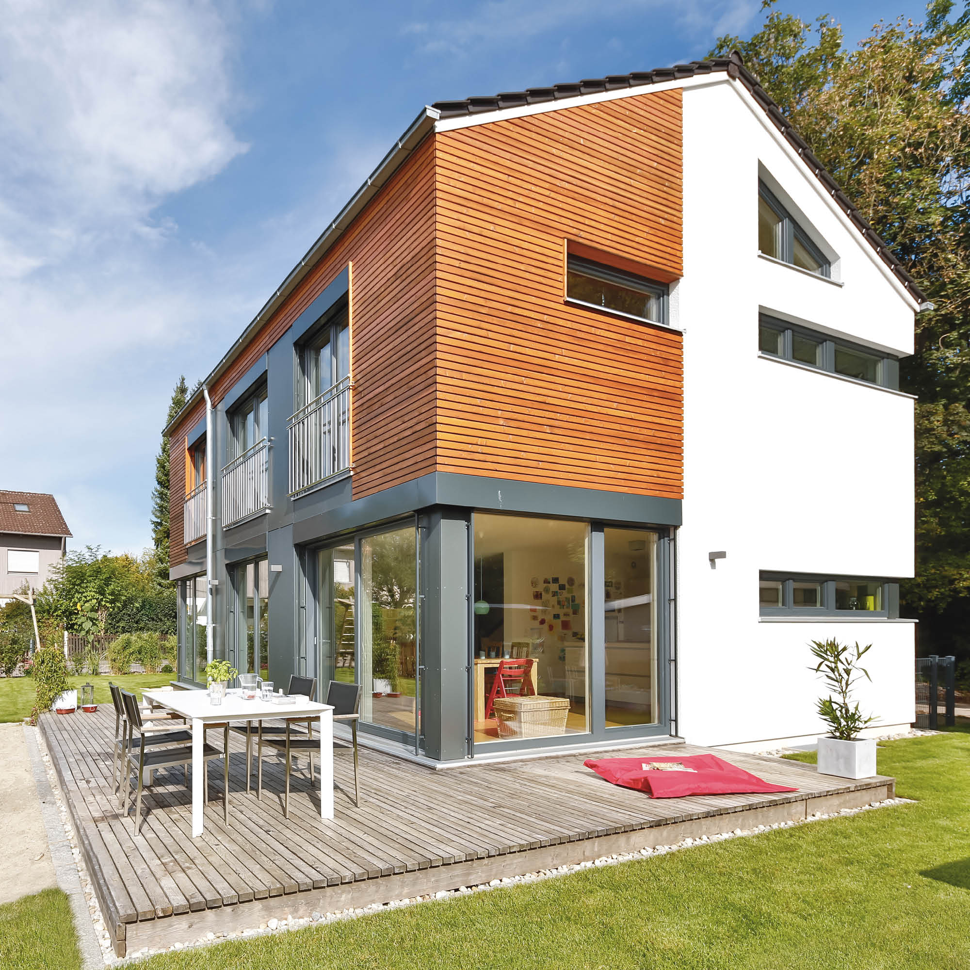 Modernes Einfamilienhaus mit Holzverkleidung und großzügiger Holzterrasse mit Esstisch.