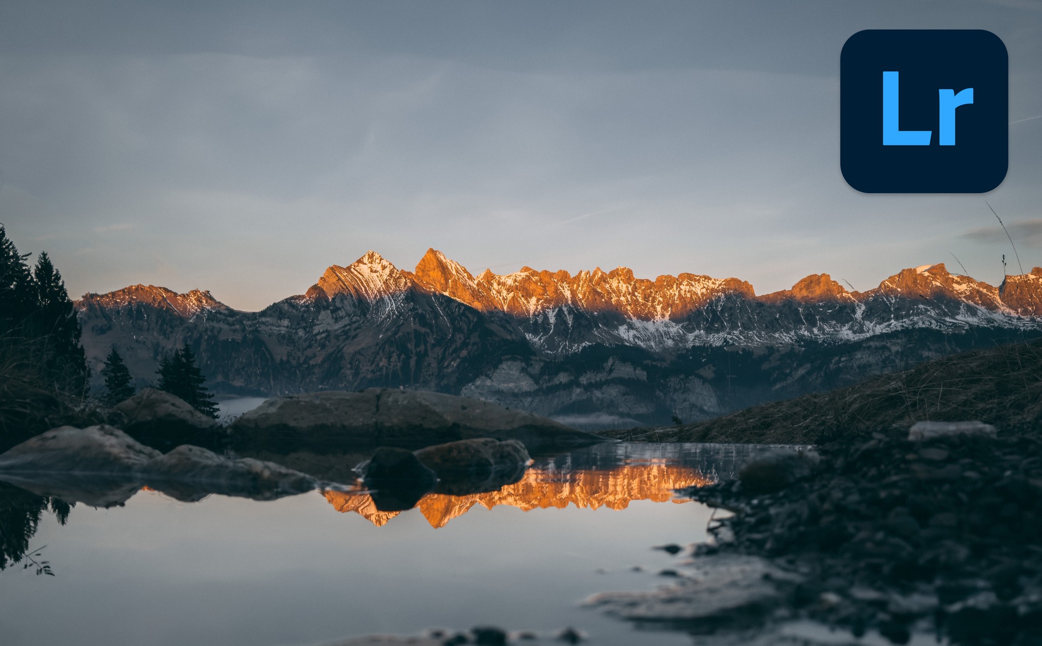 A still body of water with mountains in the background at sunset