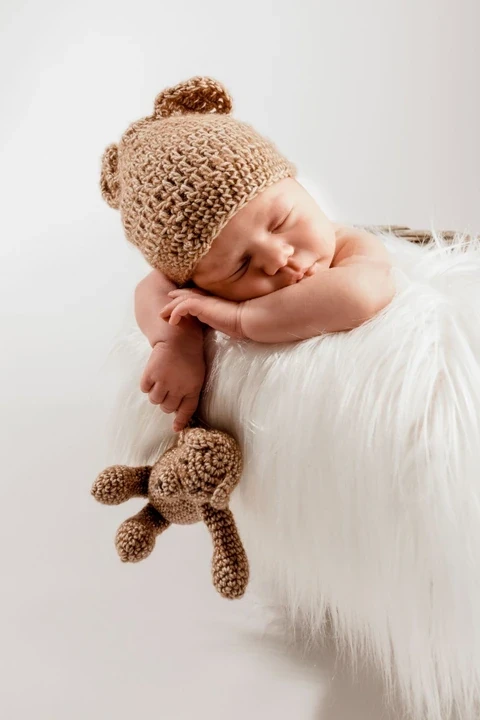 Sleeping newborn in a knitted bear hat with a small teddy bear