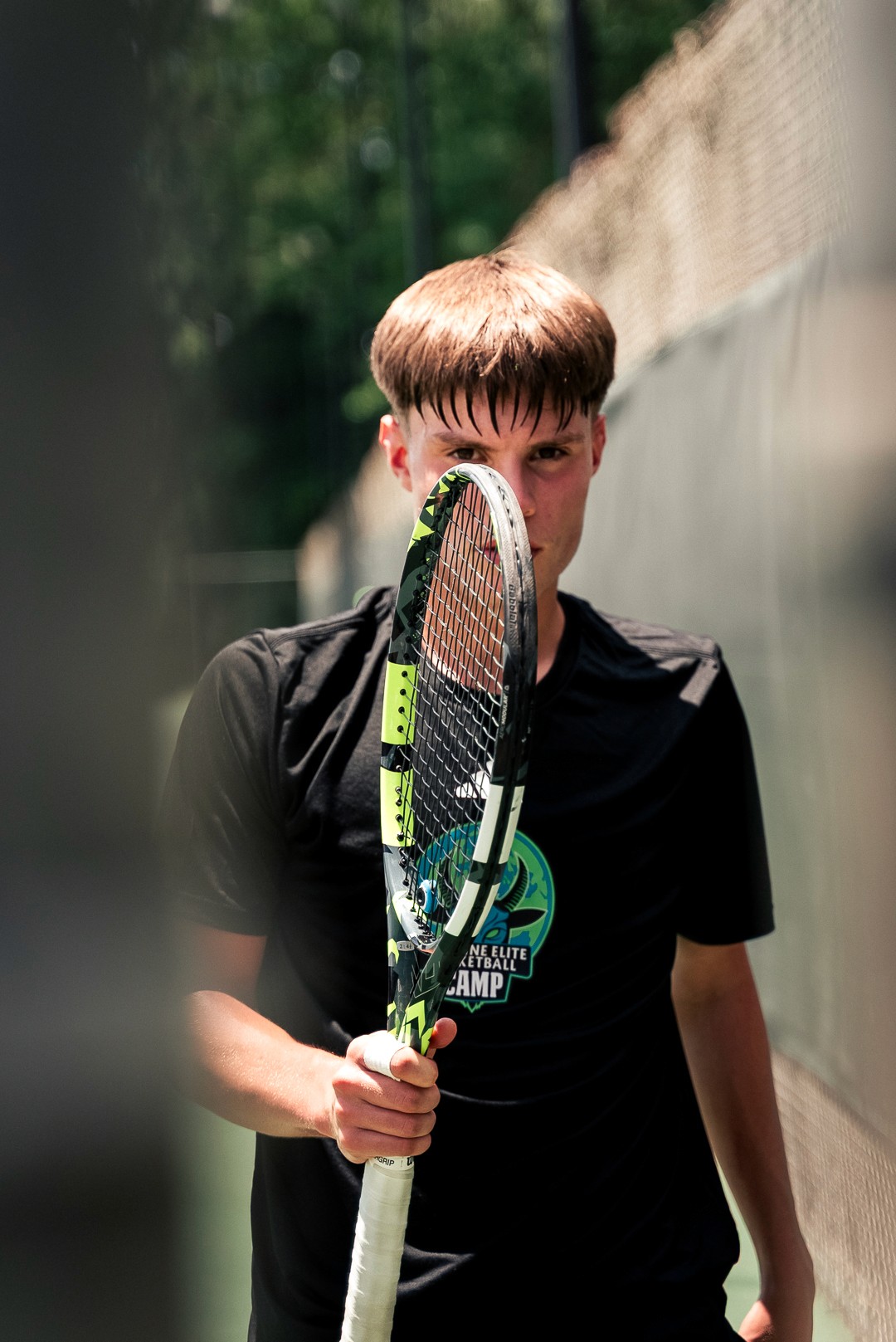 Portrait d’un joueur du Combine Elite Tennis Camp avec raquette devant le visage.