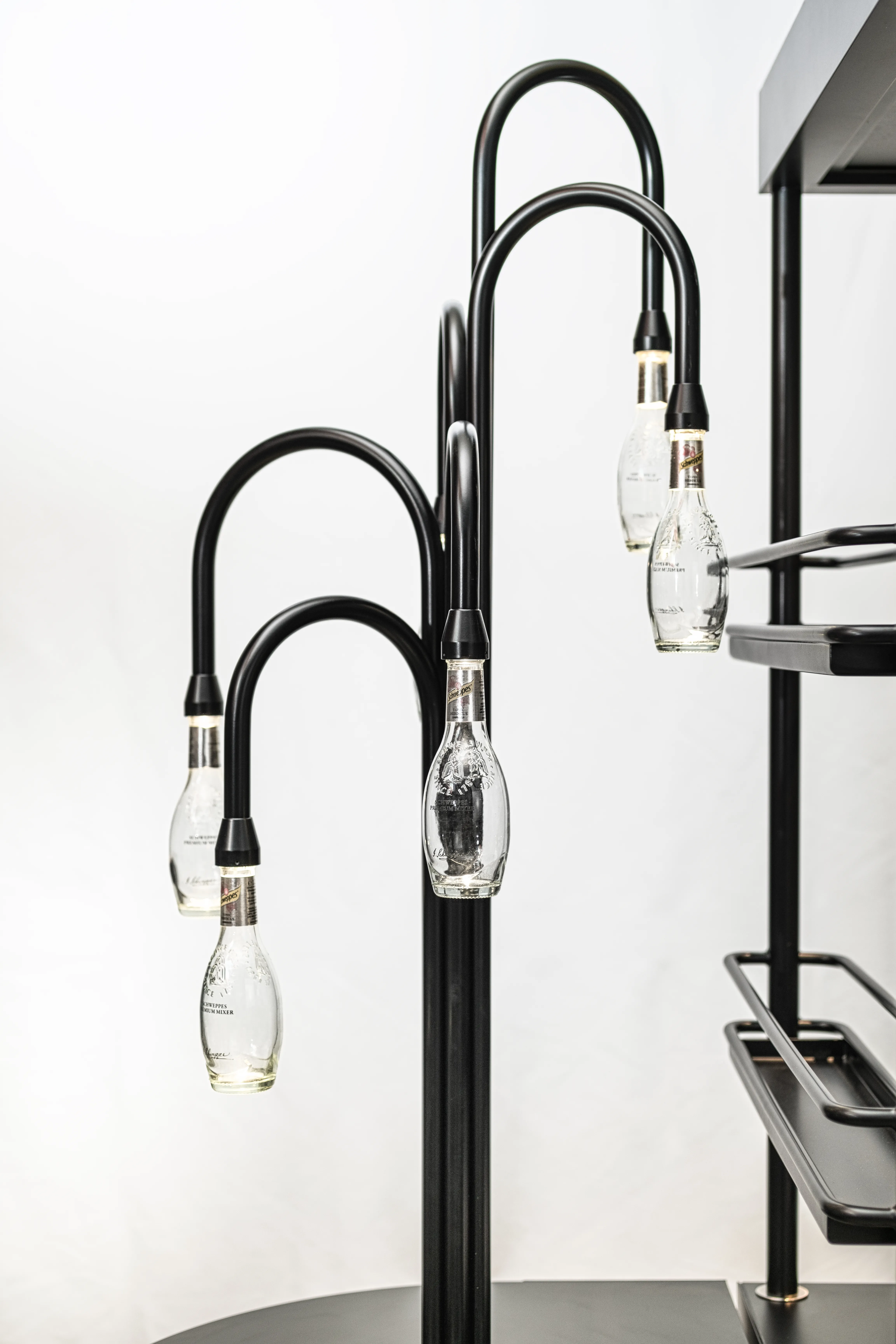 Curved black lamp arms with illuminated Schweppes bottles as lampshades on the mobile SCHWEPPES bartool.