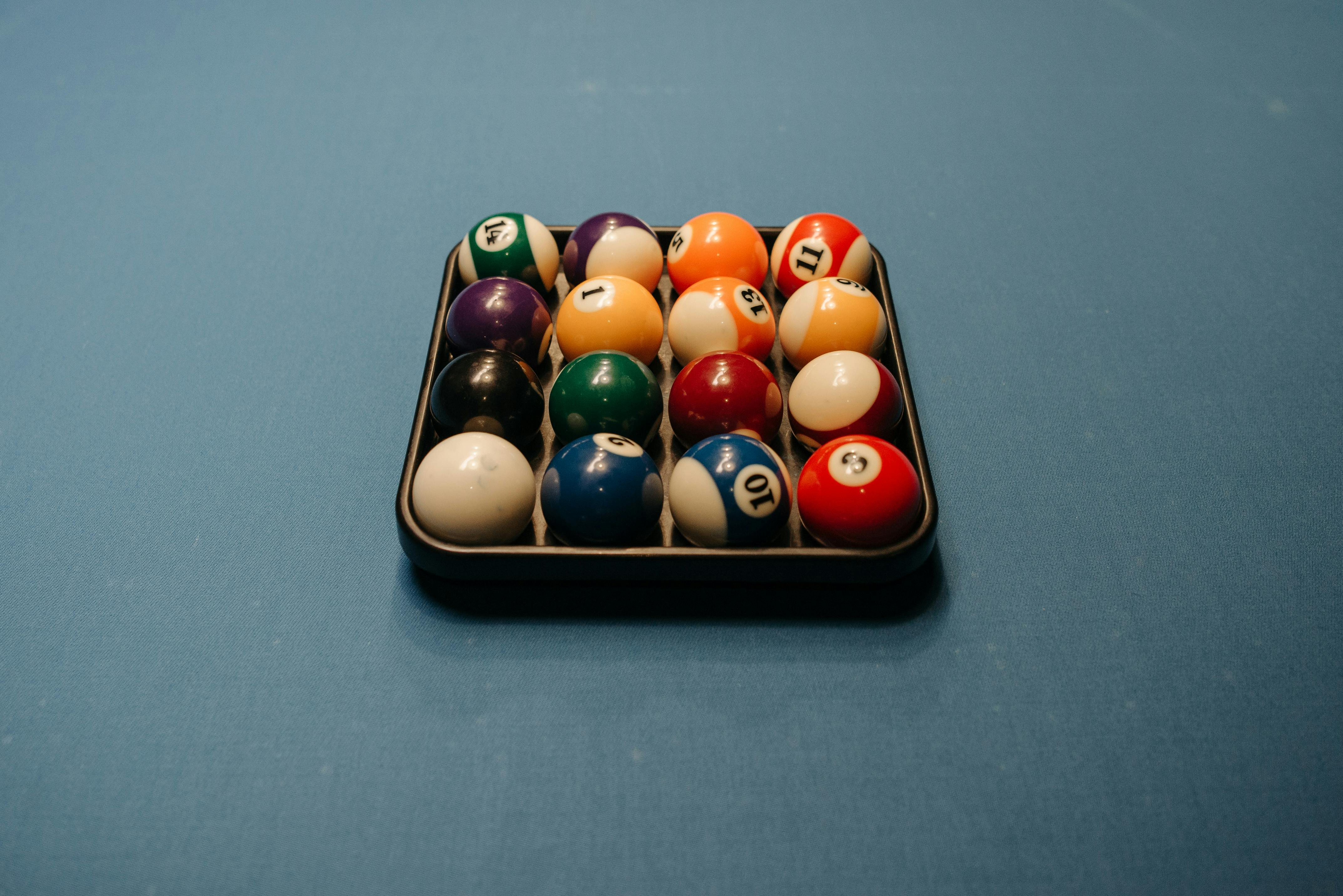 A young person with curly hair smiles at the camera while sitting in front of a laptop against a dark background.