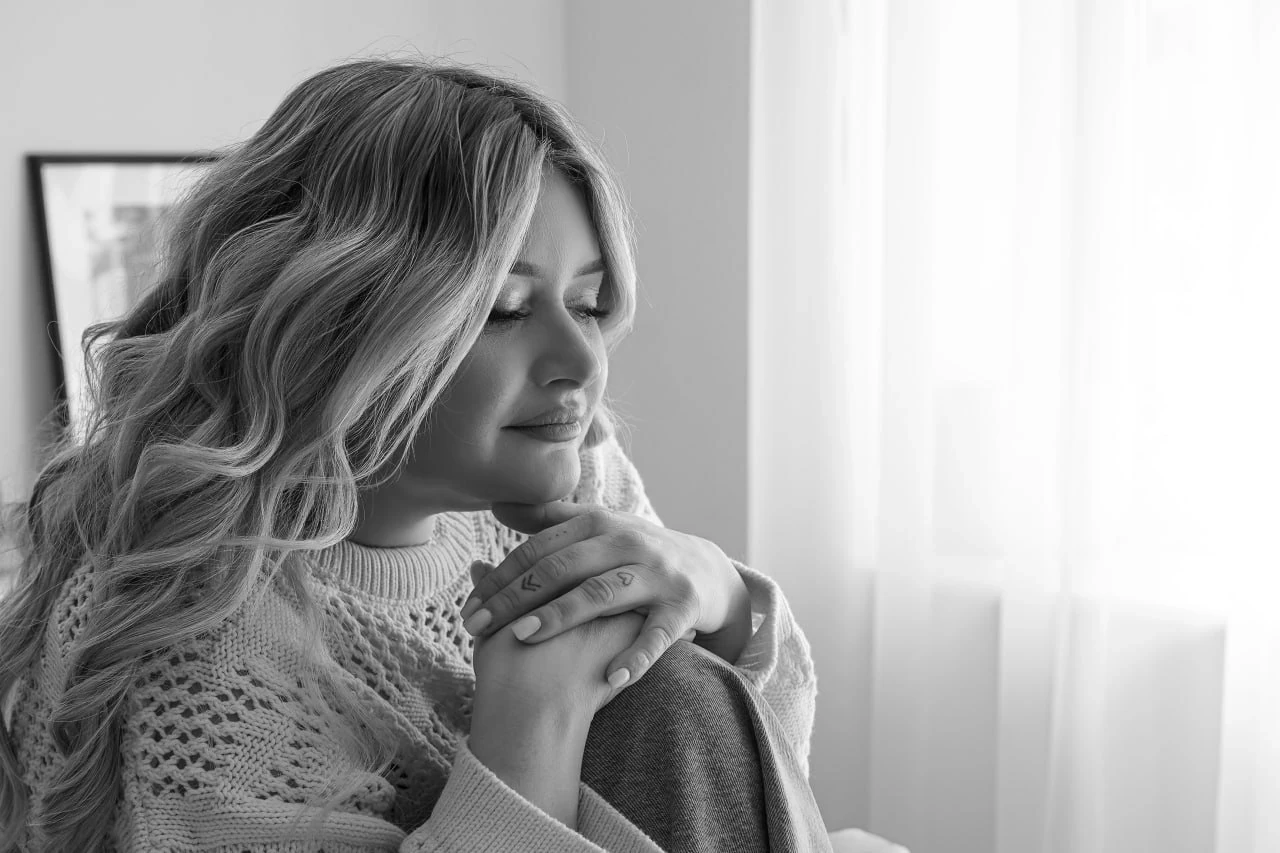  Na zdjęciu widnieje rodzina podczas pikniku na świeżym powietrzu, obok spokojnego jeziora. Składa się z mężczyzny, kobiety i małego dziecka. Mężczyzna ma na sobie jasnoniebieską koszulę i krótkie spodenki, siedzi z przodu i trzyma dziecko na kolanach. Kobieta, ubrana w kolorową sukienkę i kapelusz, siedzi obok i uśmiecha się, patrząc na dziecko. Sceneria jest zielona, z dużą ilością trawy i drzew w tle. Całość tworzy spokojną i sielankową atmosferę.