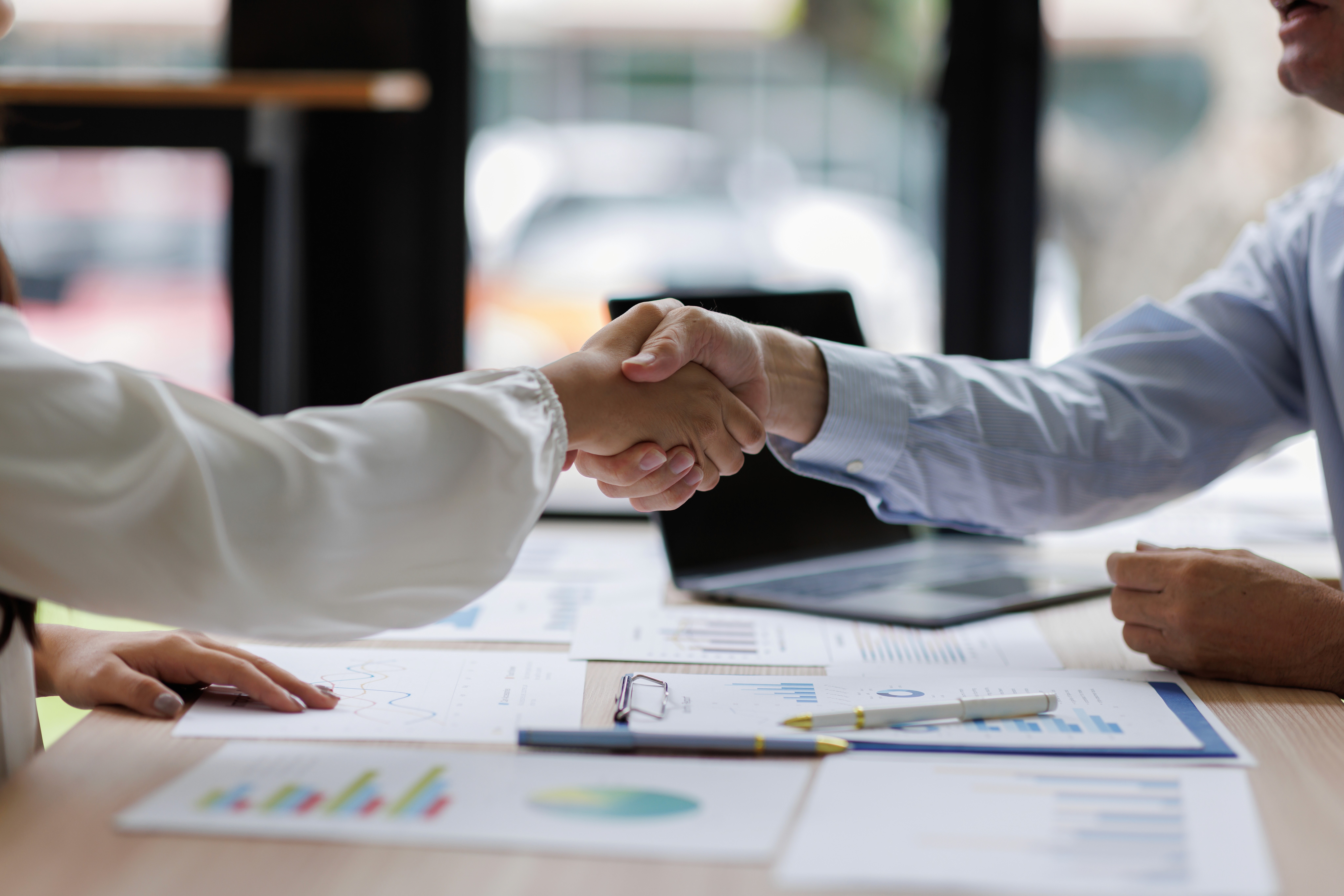 Aperto de mãos em reunião com gráficos e notebook, representando decisão financeira.