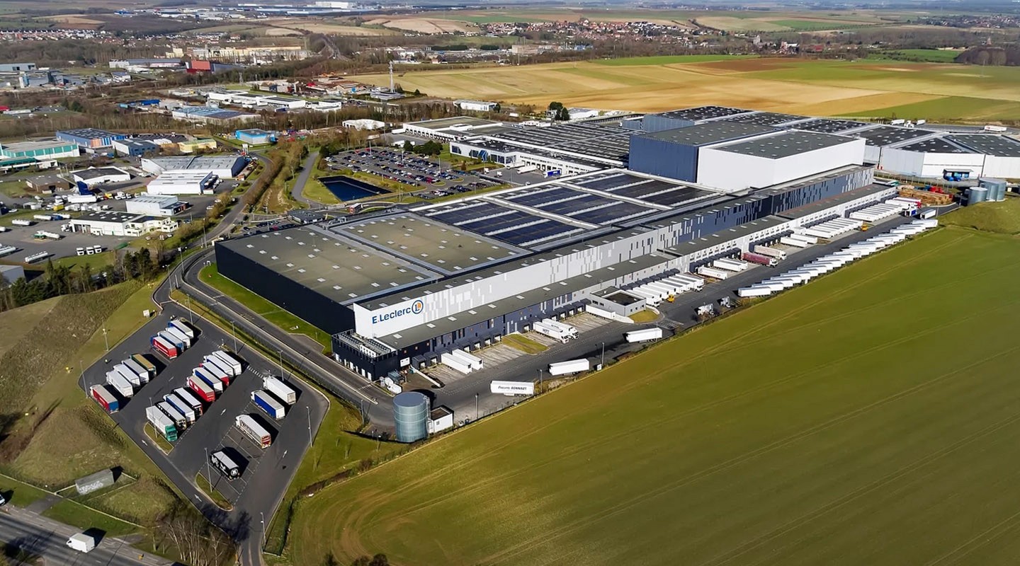 Vue aérienne d'un grand entrepôt avec des panneaux solaires sur le toit et des camions de livraison garés.