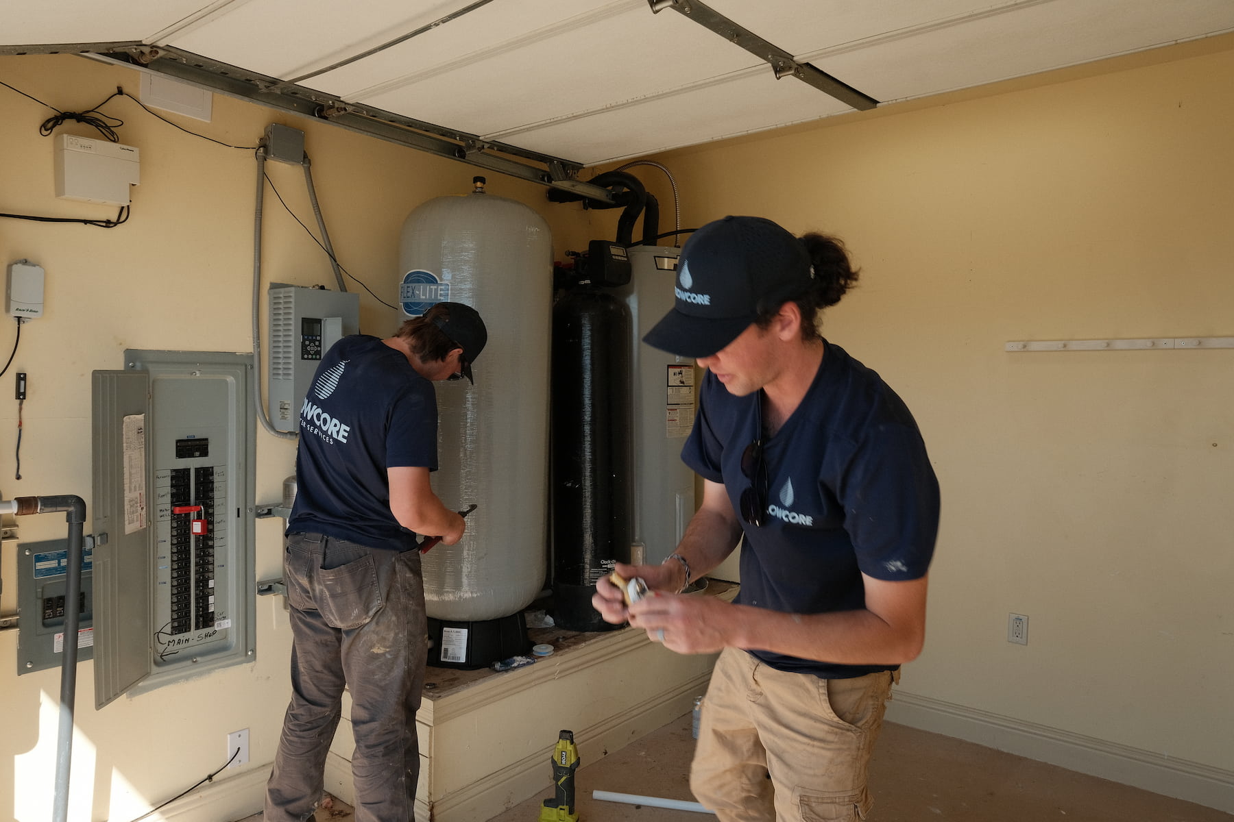 Flowcore Water Services team installing a whole-home water softener and filtration system in a residential garage in North Texas — well water treatment and conditioning services DFW
