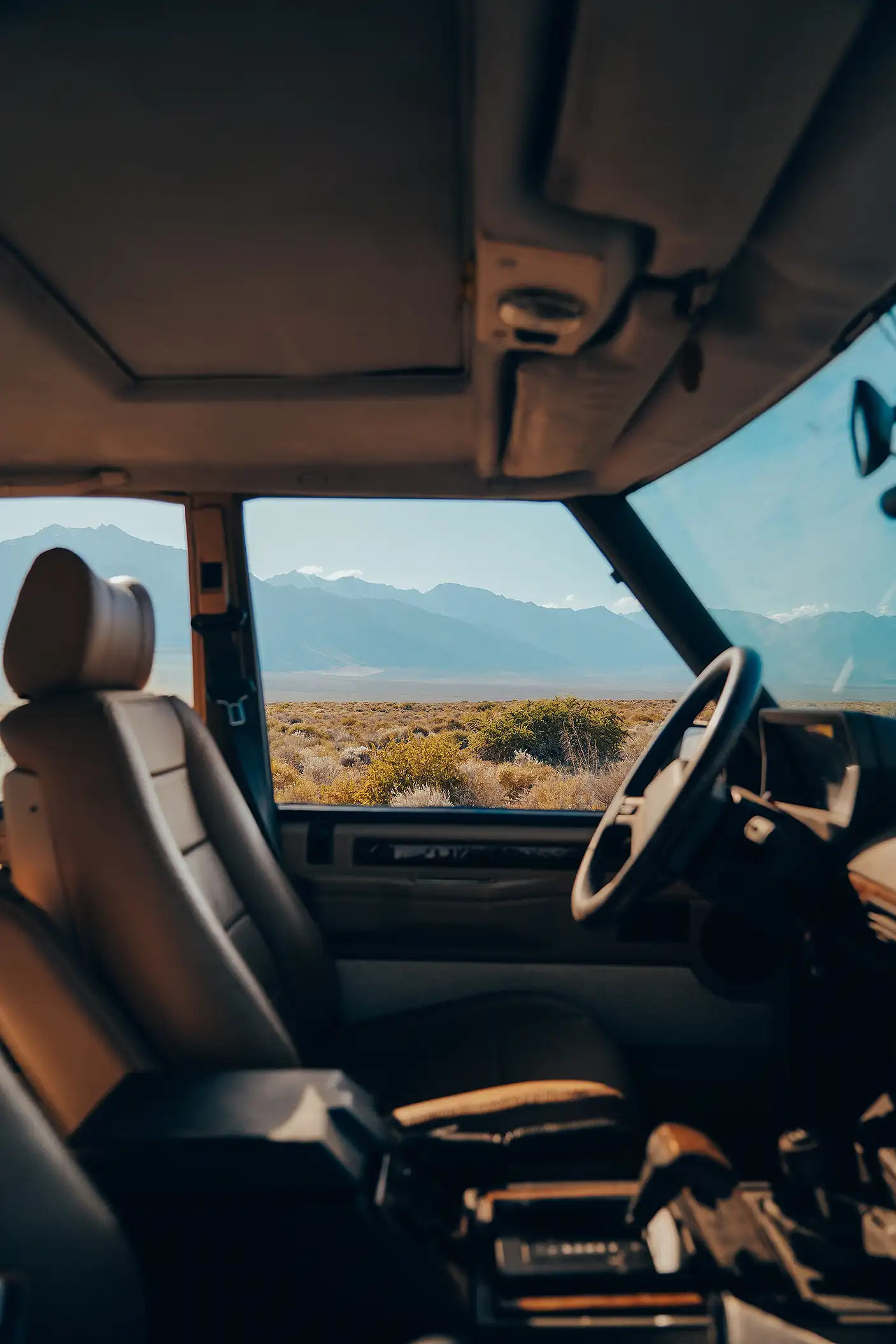 A desert landscape viewed through the driver’s side window of a silver Range Rover.