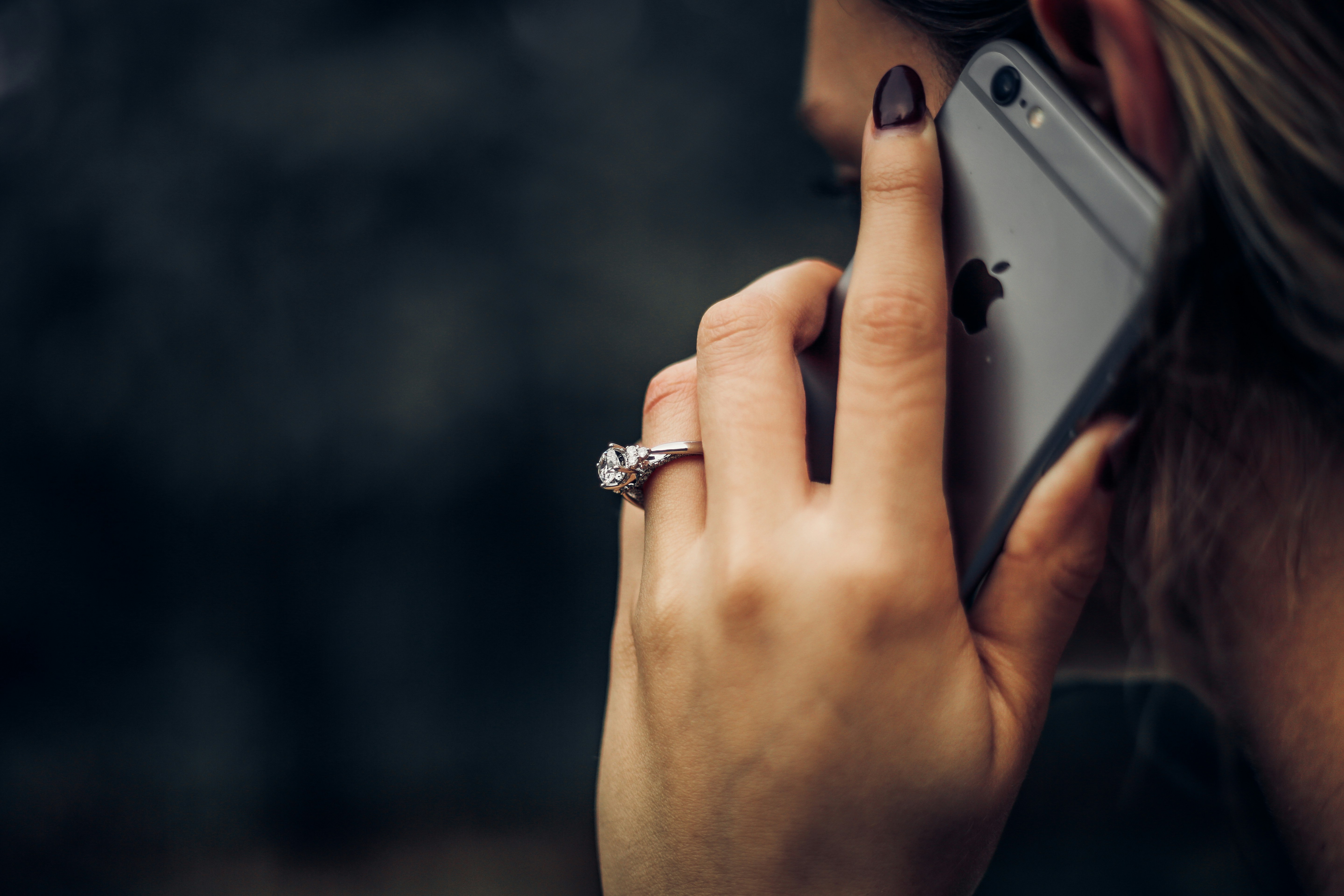 A close-up of a woman's hand holding a smartphone, wearing a ring on her finger, with a blurred background.