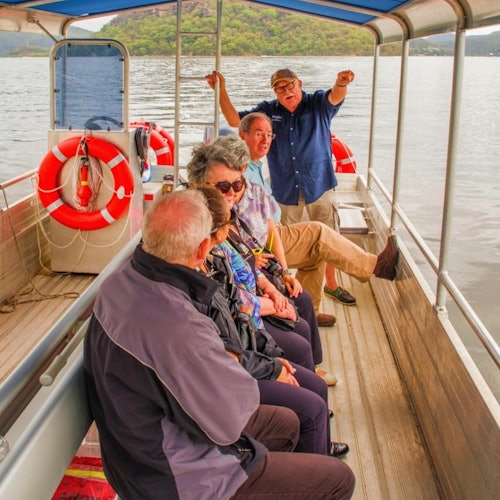 五位成年人坐在船上聊天，可以看到救生圈，背景是美丽的山景。