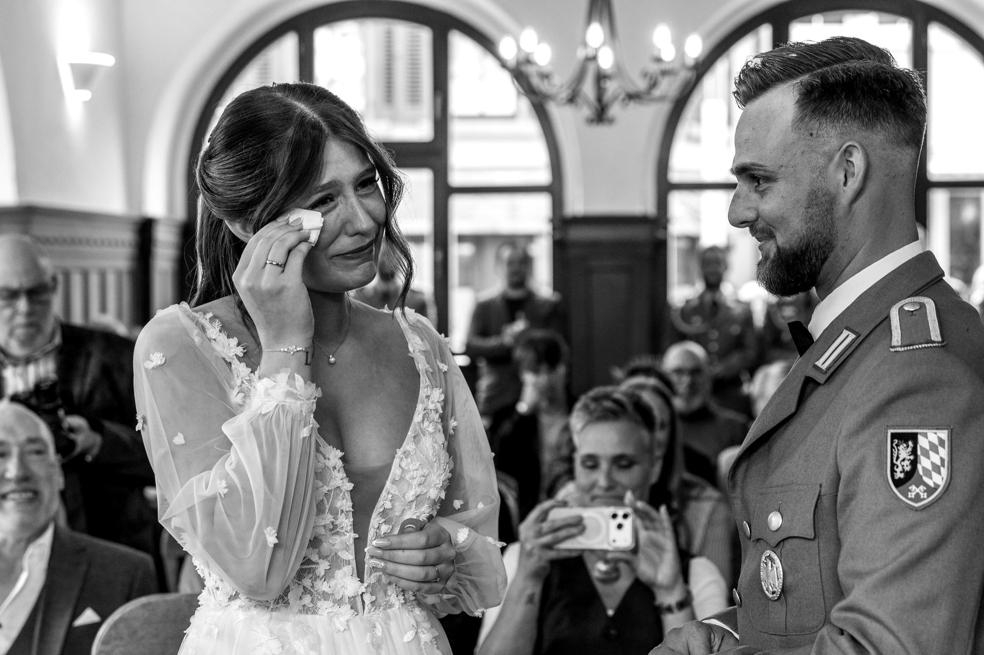 Paula wischt sich bei der Trauung eine Träne weg, Bastian lächelt sie an. Schwarzweißfoto
