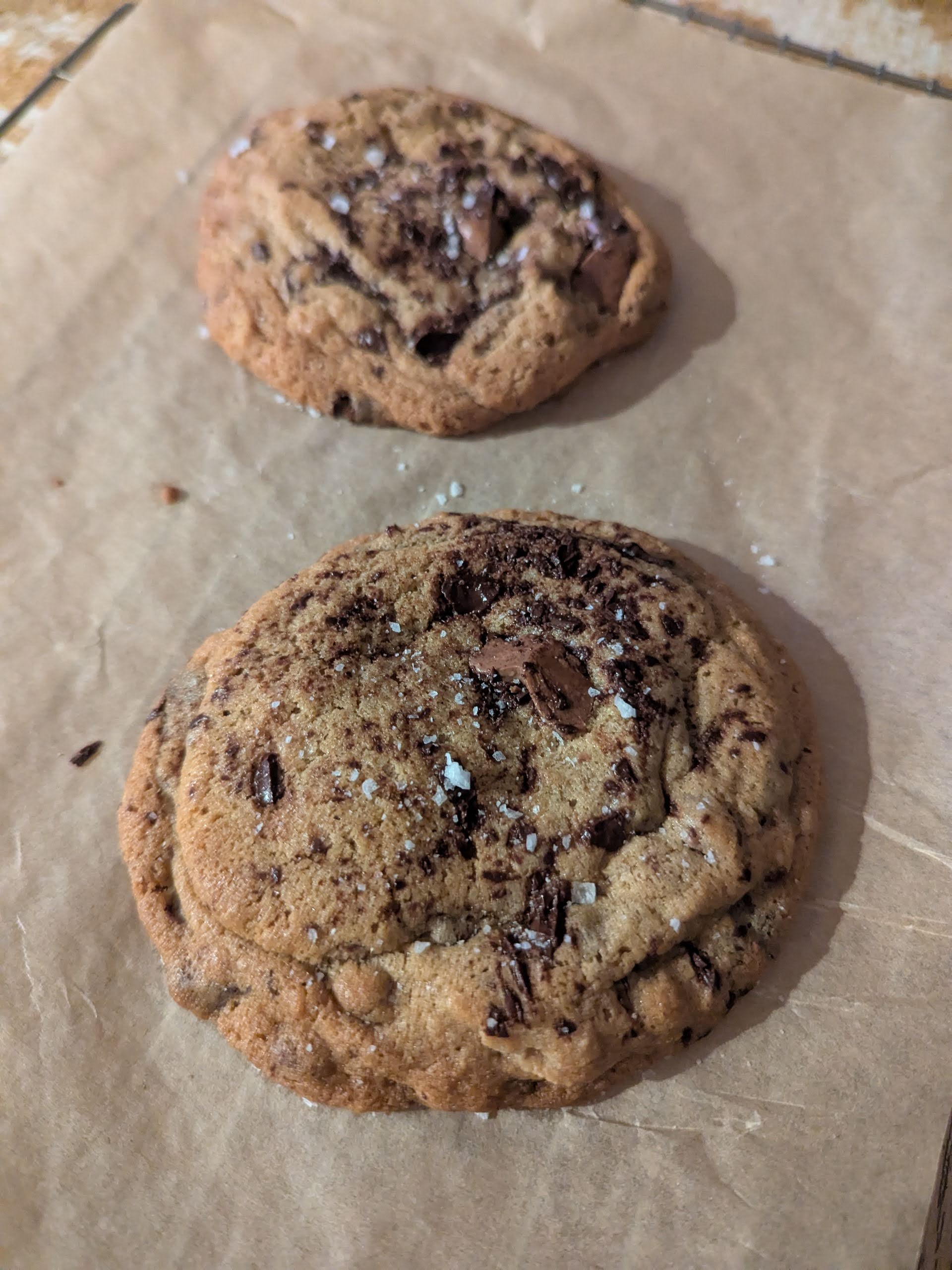 two chocolate chip cookies on baking paper with a pinch of sea salt flakes