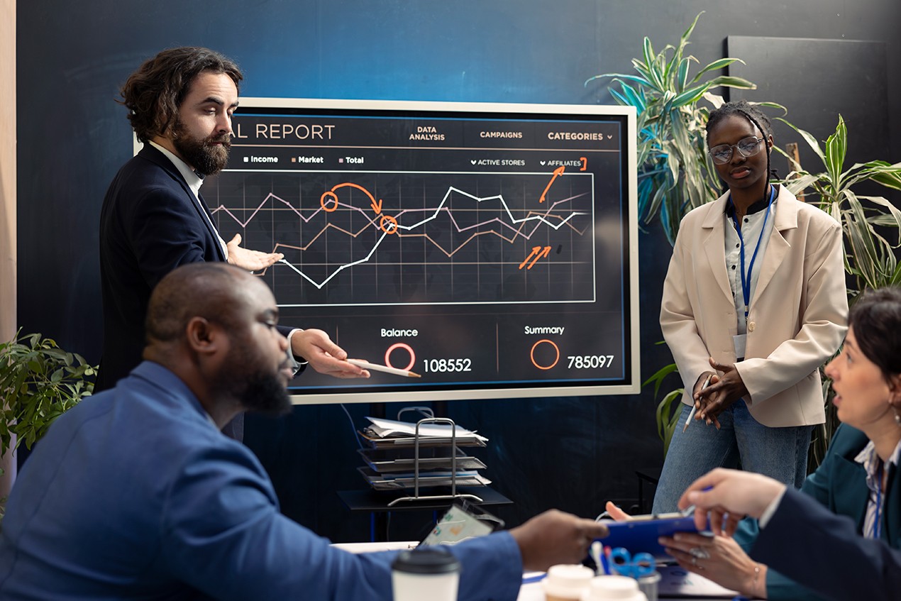 Man presenting charts on a large screen to audience.