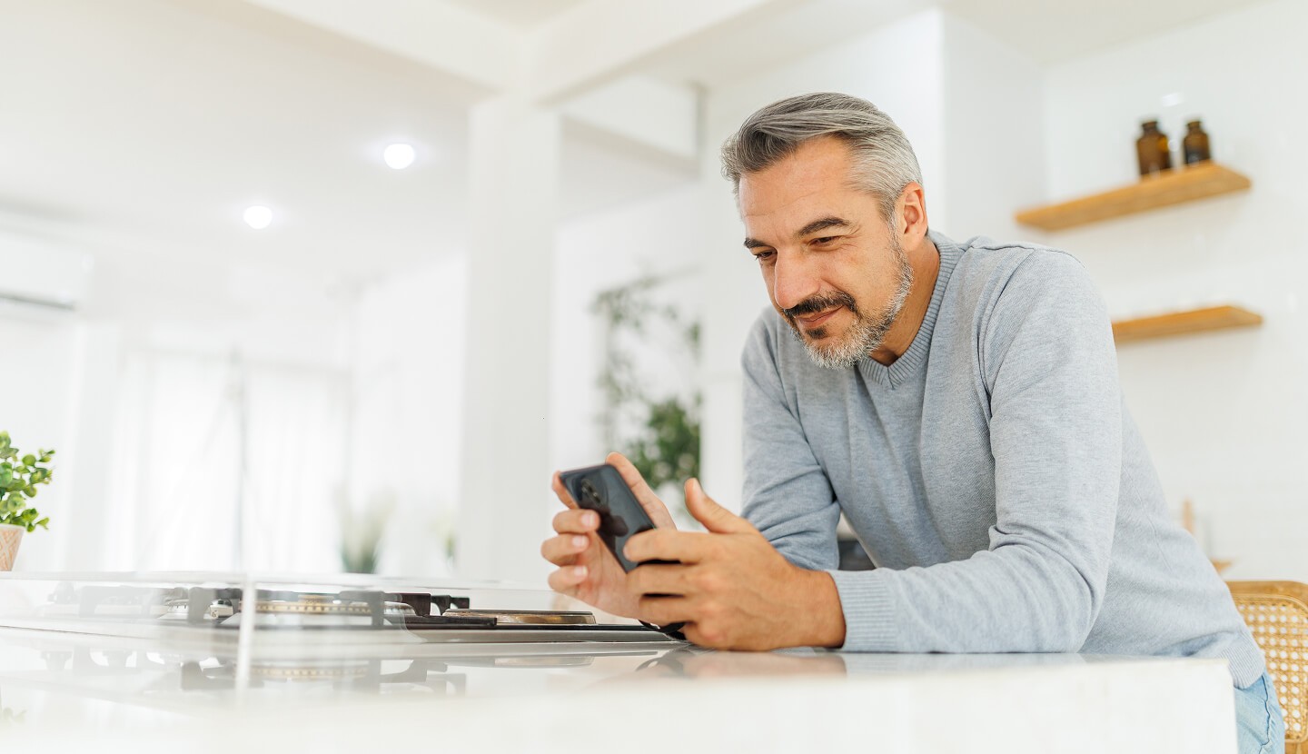 Older man looking at his phone in the kitchen.