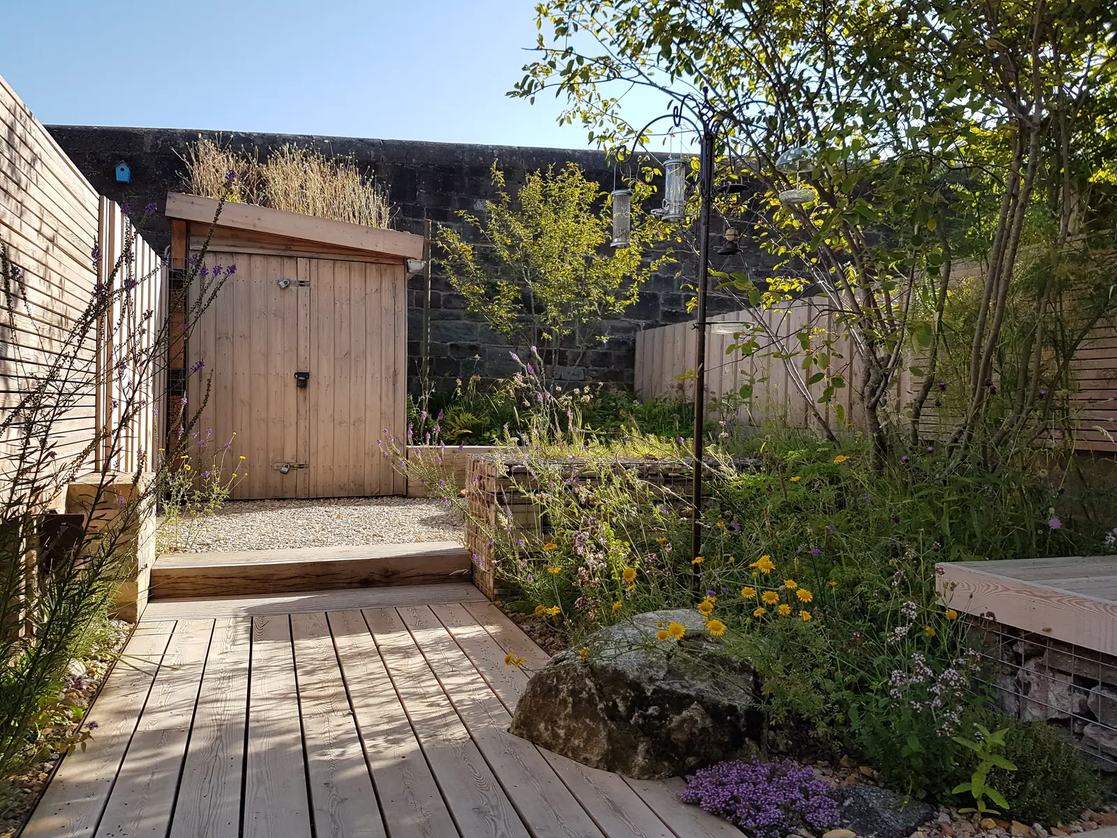Pathway leading through a serene garden, featuring greenery and stone walls under a clear blue sky.