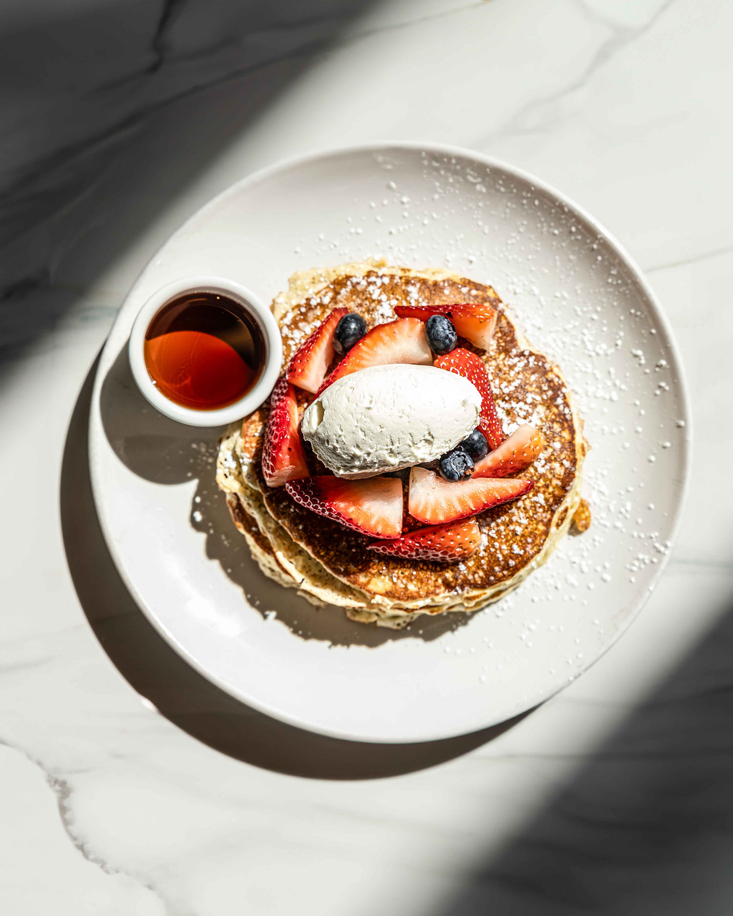 Fluffy pancakes topped with fresh strawberries, blueberries, and whipped butter, served with warm syrup at Hubbard Inn Chicago — a brunch essential.