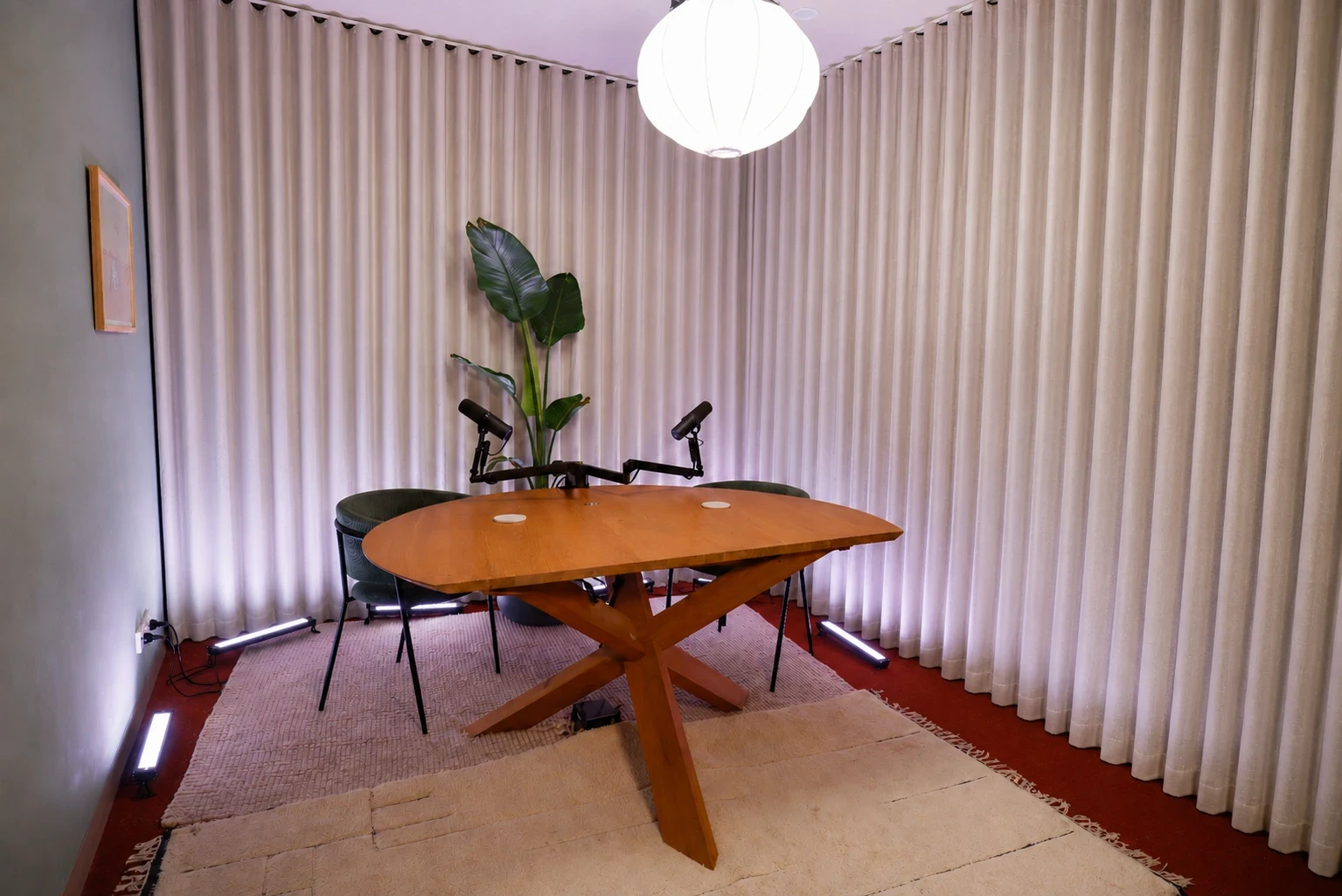 ARC set — a round wooden table with chairs and microphones, a plant and warm curtains, lit by a paper lantern