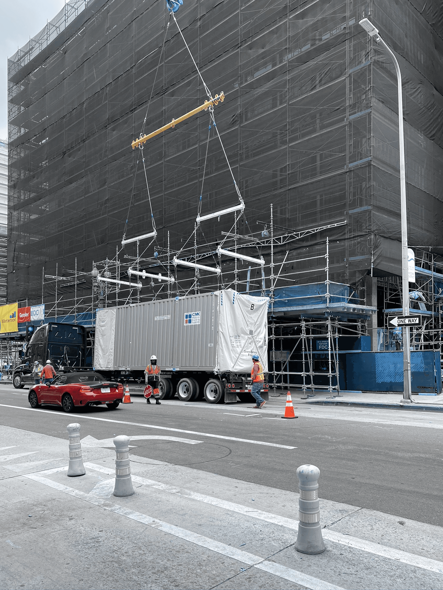 Photo of a guestroom module on a flatbed truck, with a crane positioning it for attachment and lifting into place.