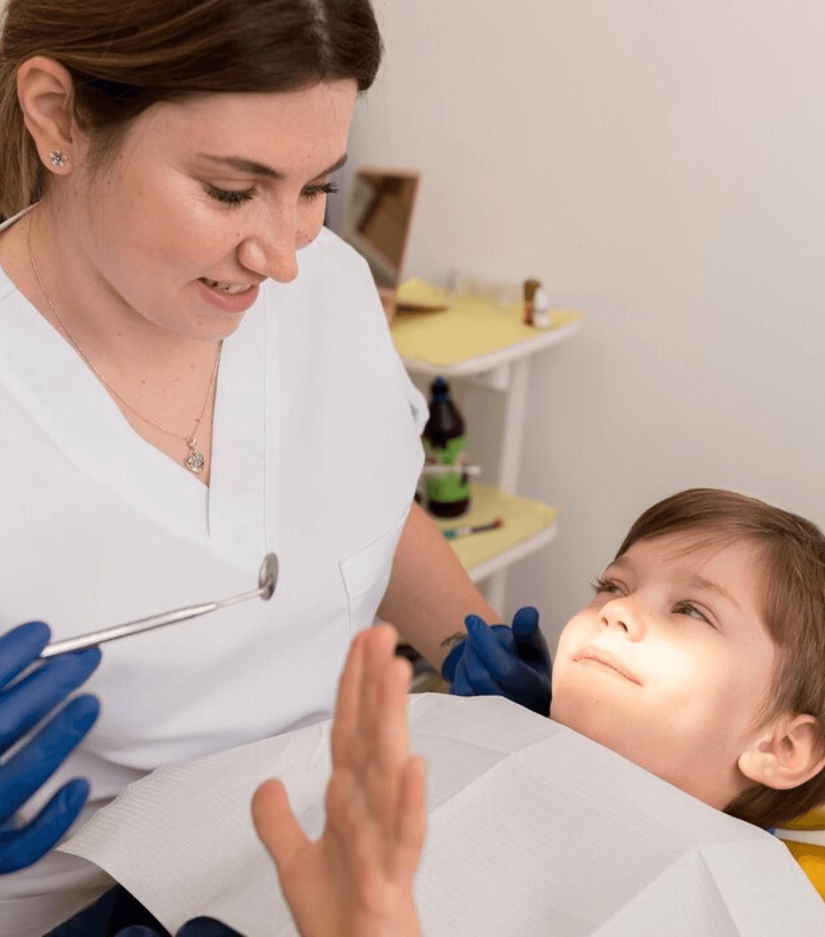 A dentist interacting with a young child in a dental chair, both smiling and engaging in a positive dental experience.