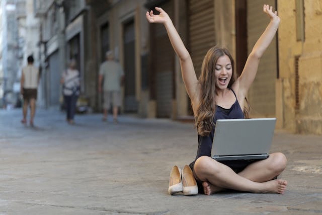 Woman sitting on the street with raised hands and a laptop in her lap