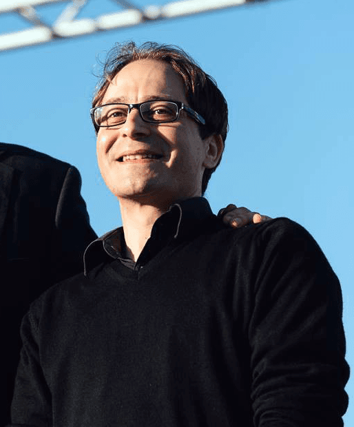 Scientist wearing safety goggles and blue lab attire, using a pipette to transfer liquid into a vial in a laboratory setting.