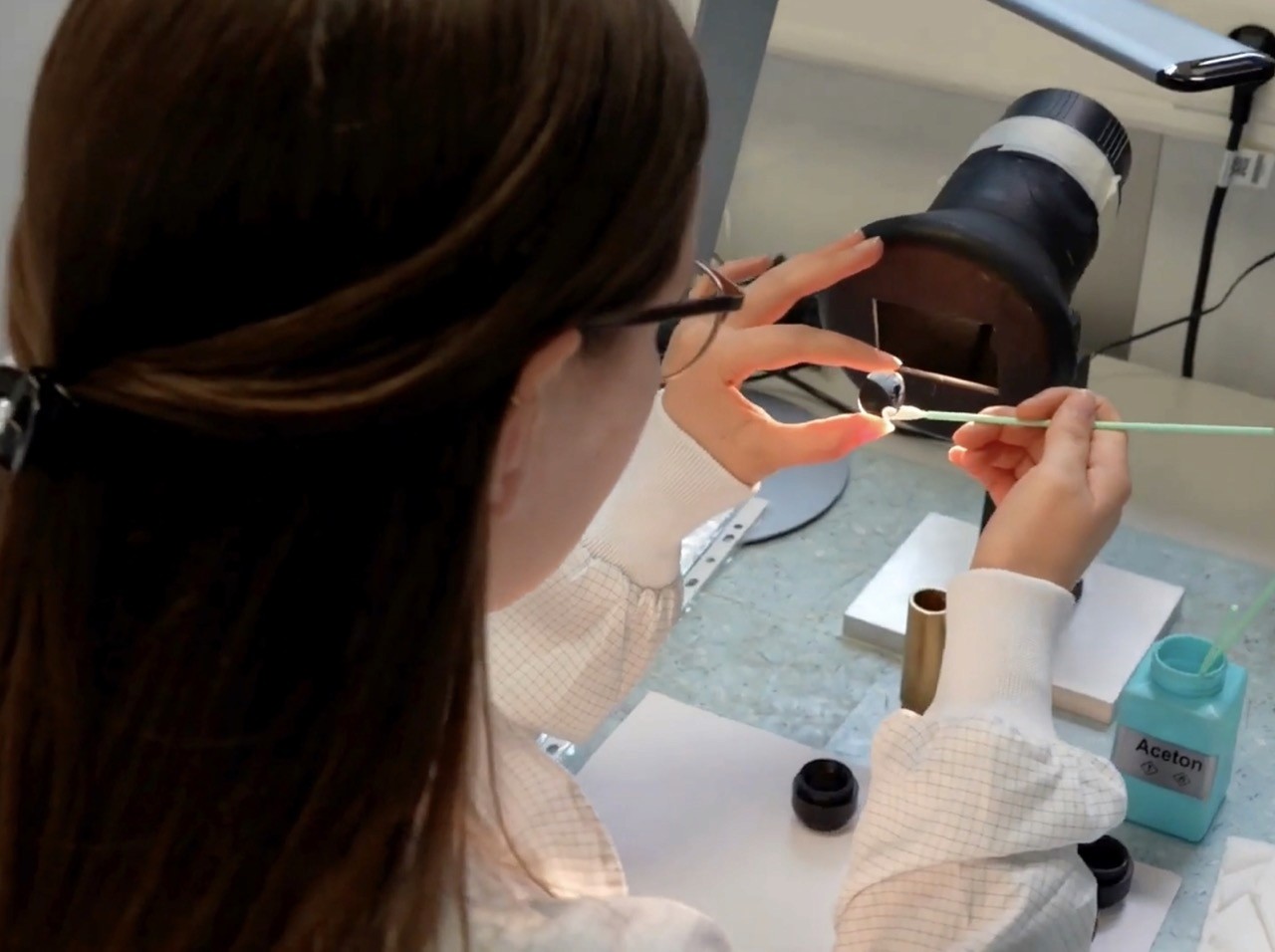 Person cleaning lens with swab under light fixture, "Acetone" label visible. Karl Kaps.