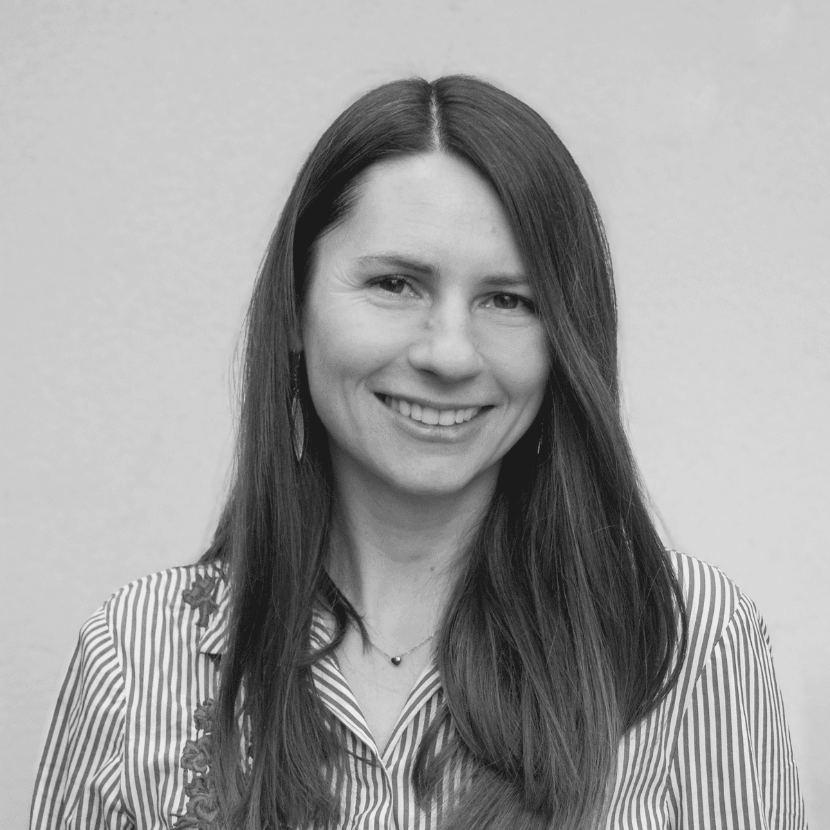 A person with wavy light hair stands facing slightly to the left, wearing a striped shirt against a neutral background.