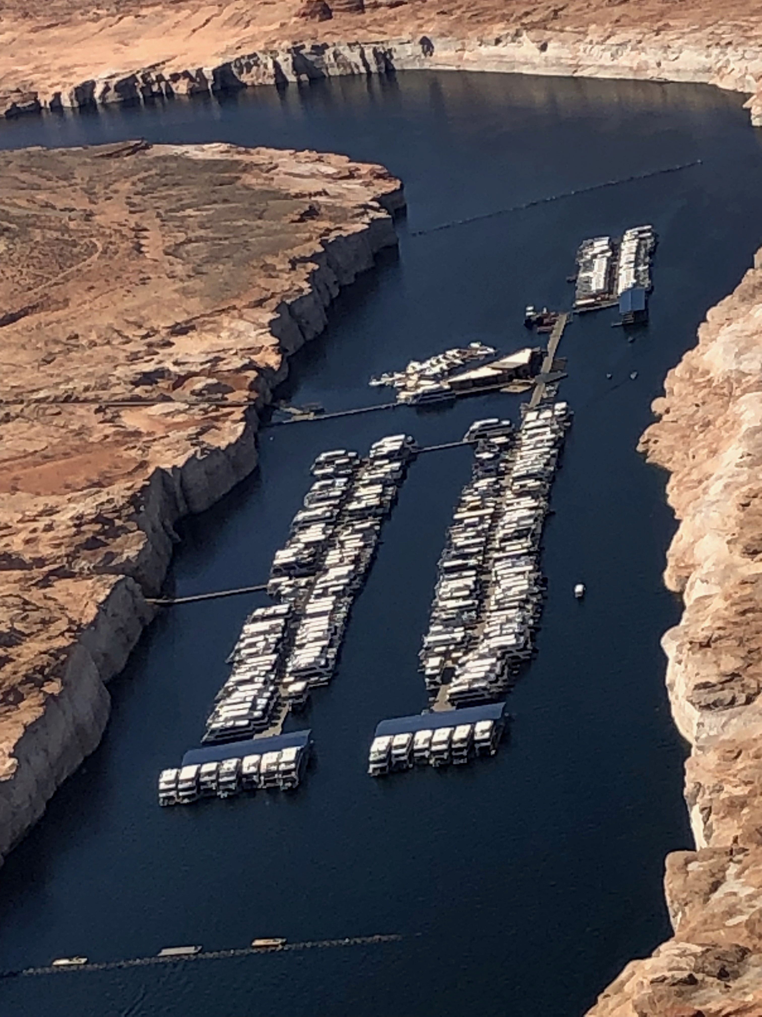 Aerial view of Antelope Point Marina on Lake Powell, rows of houseboats in a narrow channel with a wide white mineral band on the canyon walls above the water.