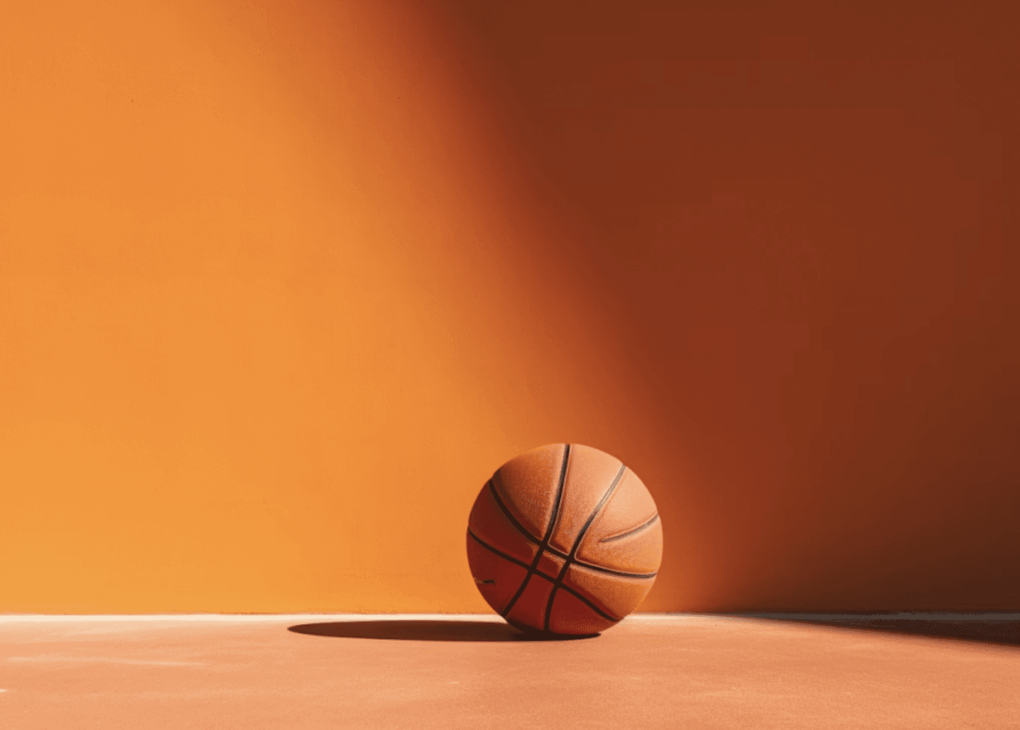 A minimalist photograph of a basketball sitting on a smooth floor, with a dramatic, single light source casting a long, distinct shadow to the left.