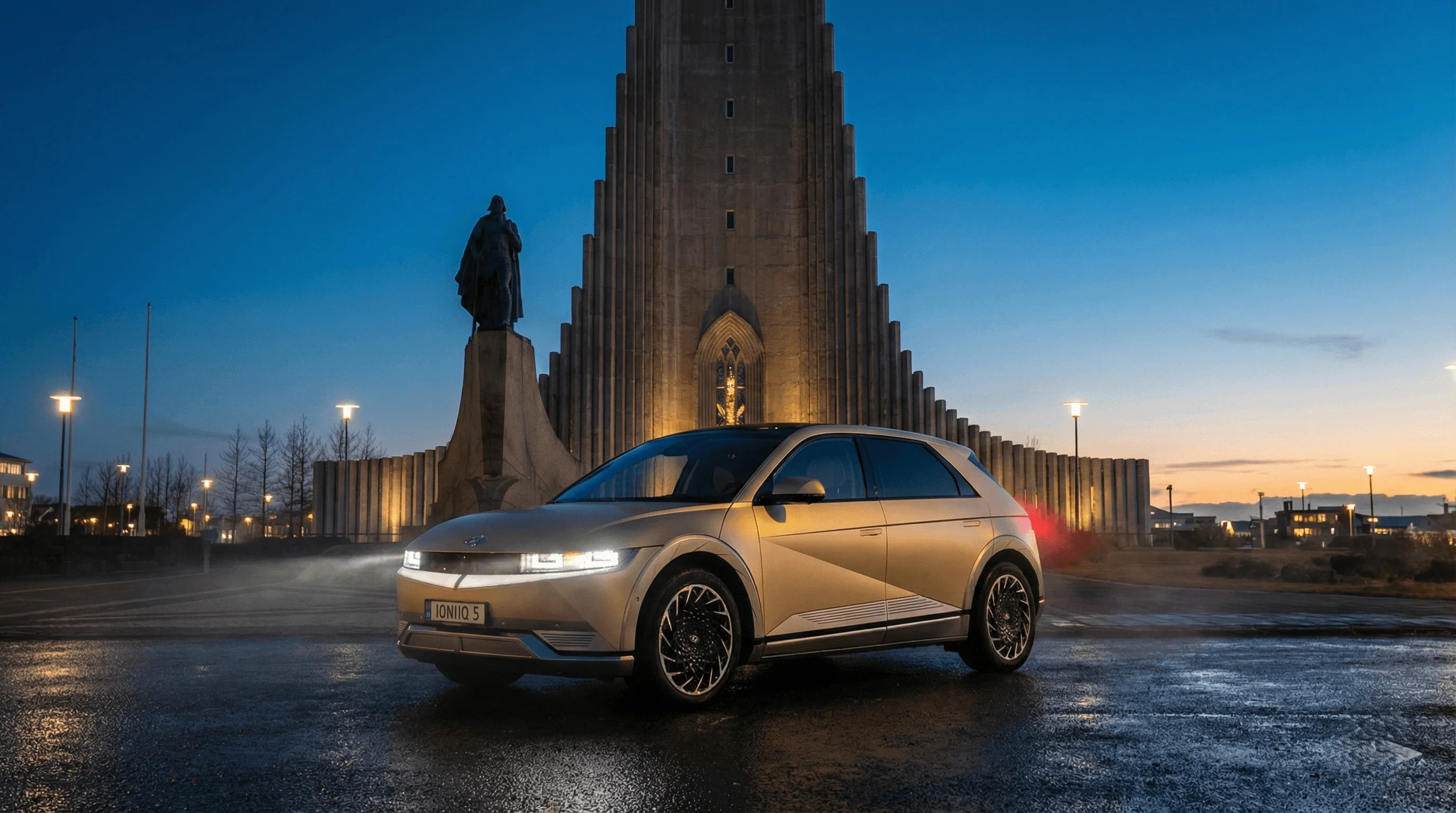 A beige electric SUV parked at night in front of the illuminated Hallgrímskirkja church.