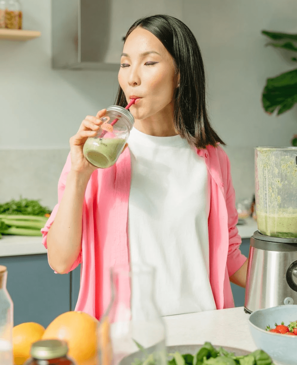 Asian woman sipping a green smoothie in a modern kitchen setting