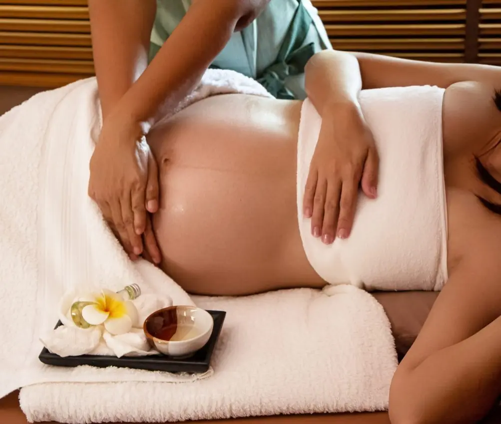 A woman lying down with a towel wrapped around her head, her face glowing with facial oil. She has a peaceful expression, enjoying a skincare treatment.