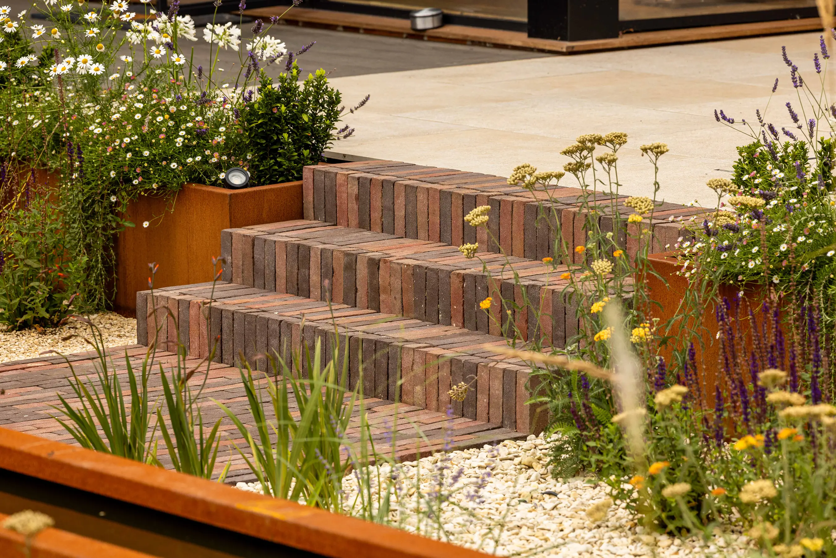 A close-up of stone steps leading through a lush, green garden with blooming flowers on either side.