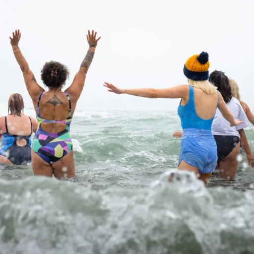 Group of friends enjoying wild swimming together in ocean waves with raised arms