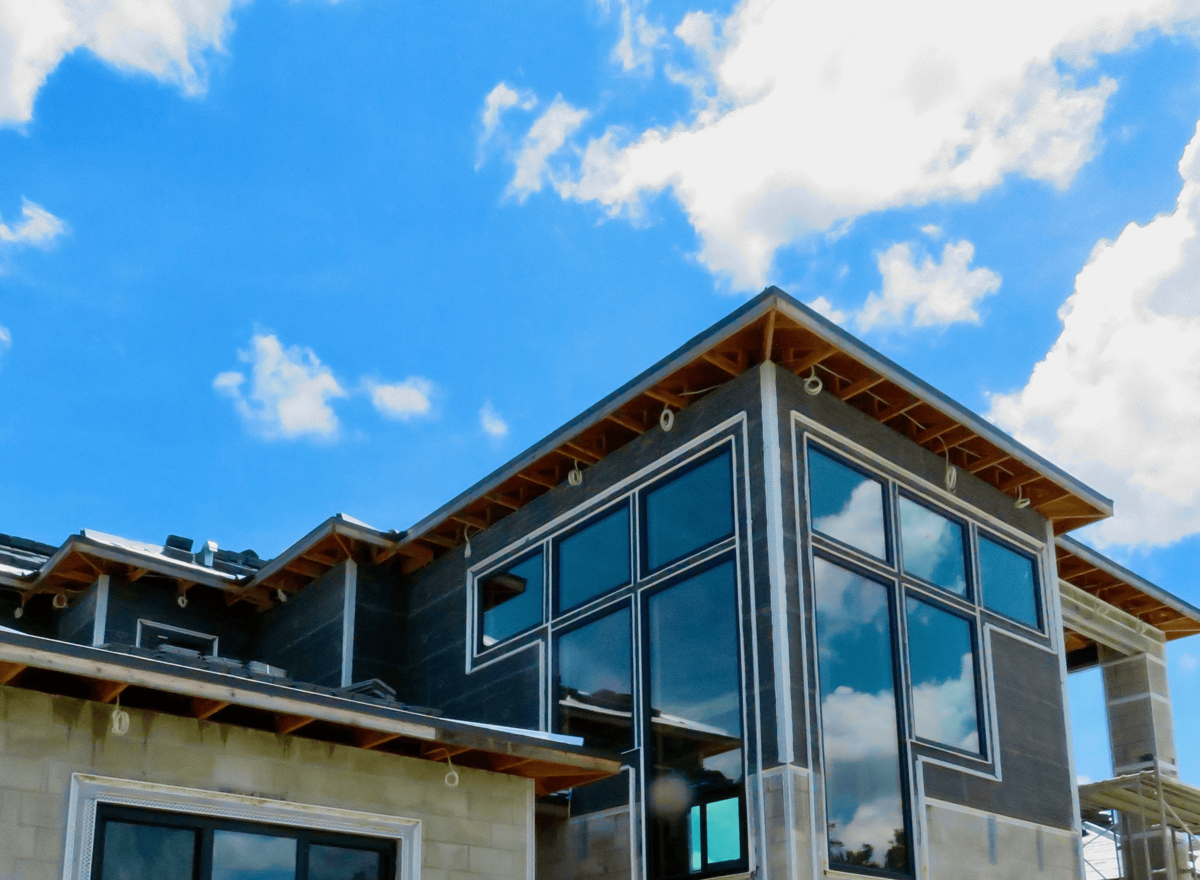 Modern house construction with large windows reflecting the blue sky.