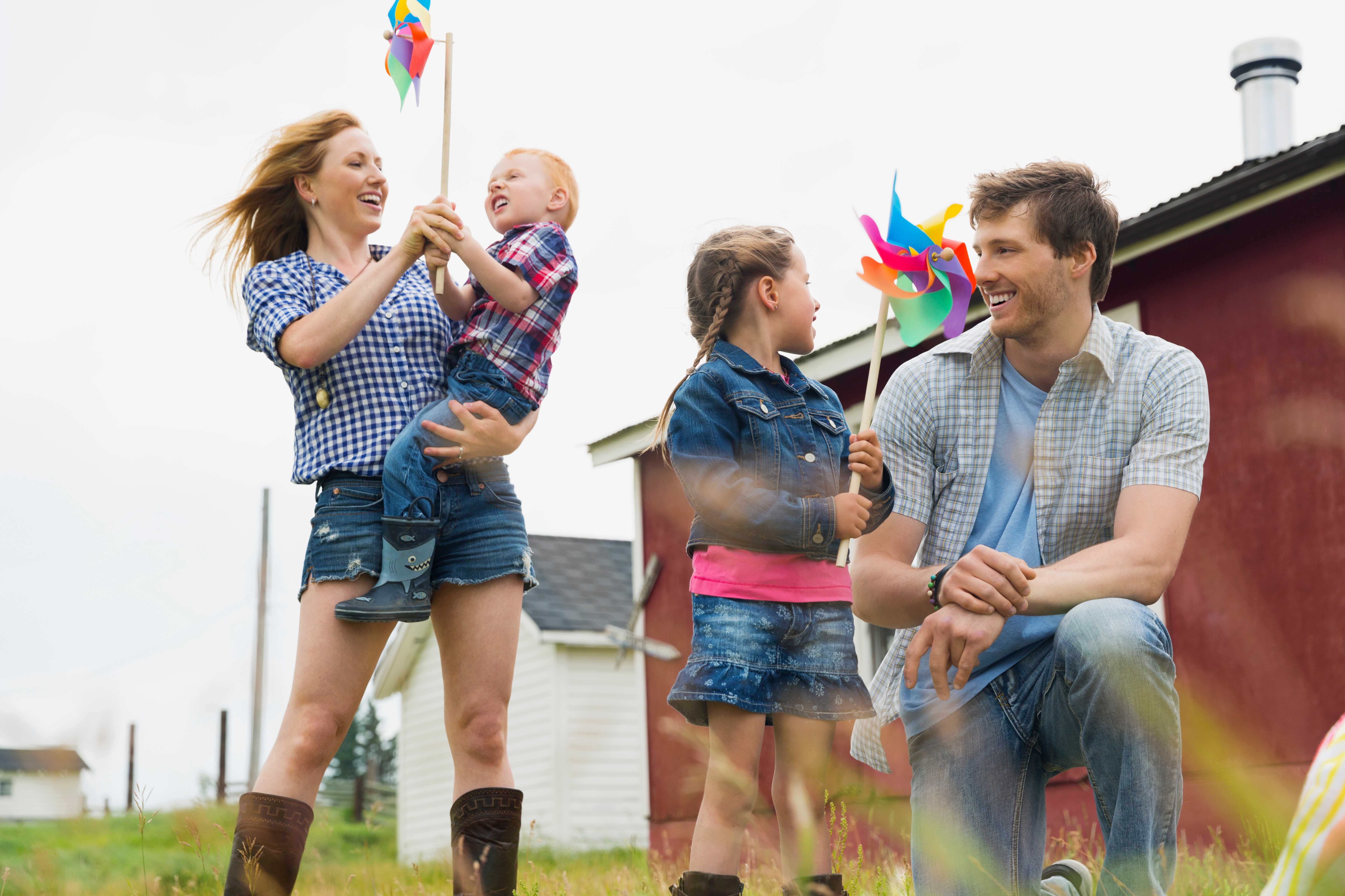 Junge Familie spielt fröhlich im Freien – Eltern und Kinder halten bunte Windräder und genießen gemeinsame Zeit auf dem Land.