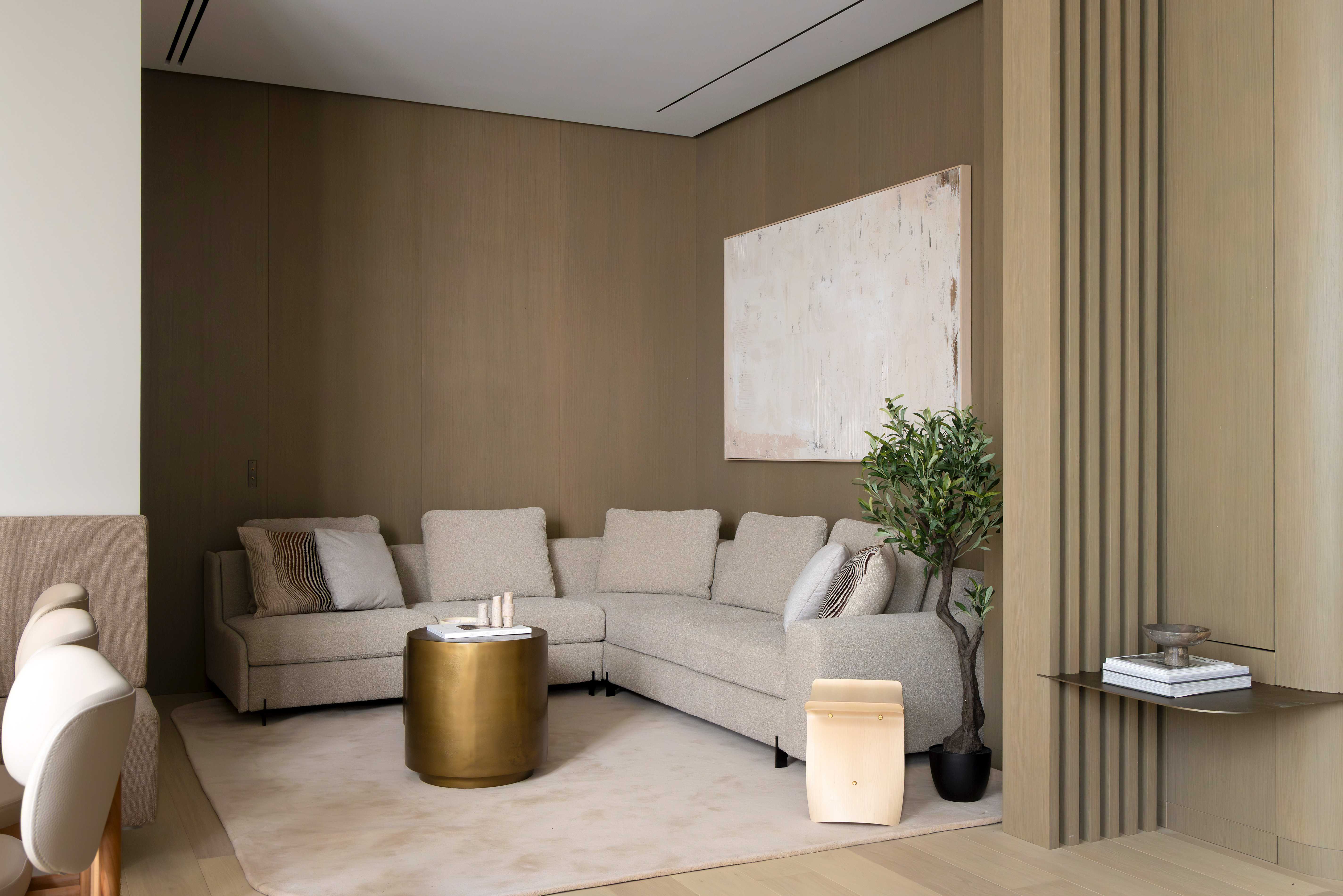 Salon vu de l'entree avec canape d'angle beige, table basse doree, tableau abstrait, plante et claustra bois