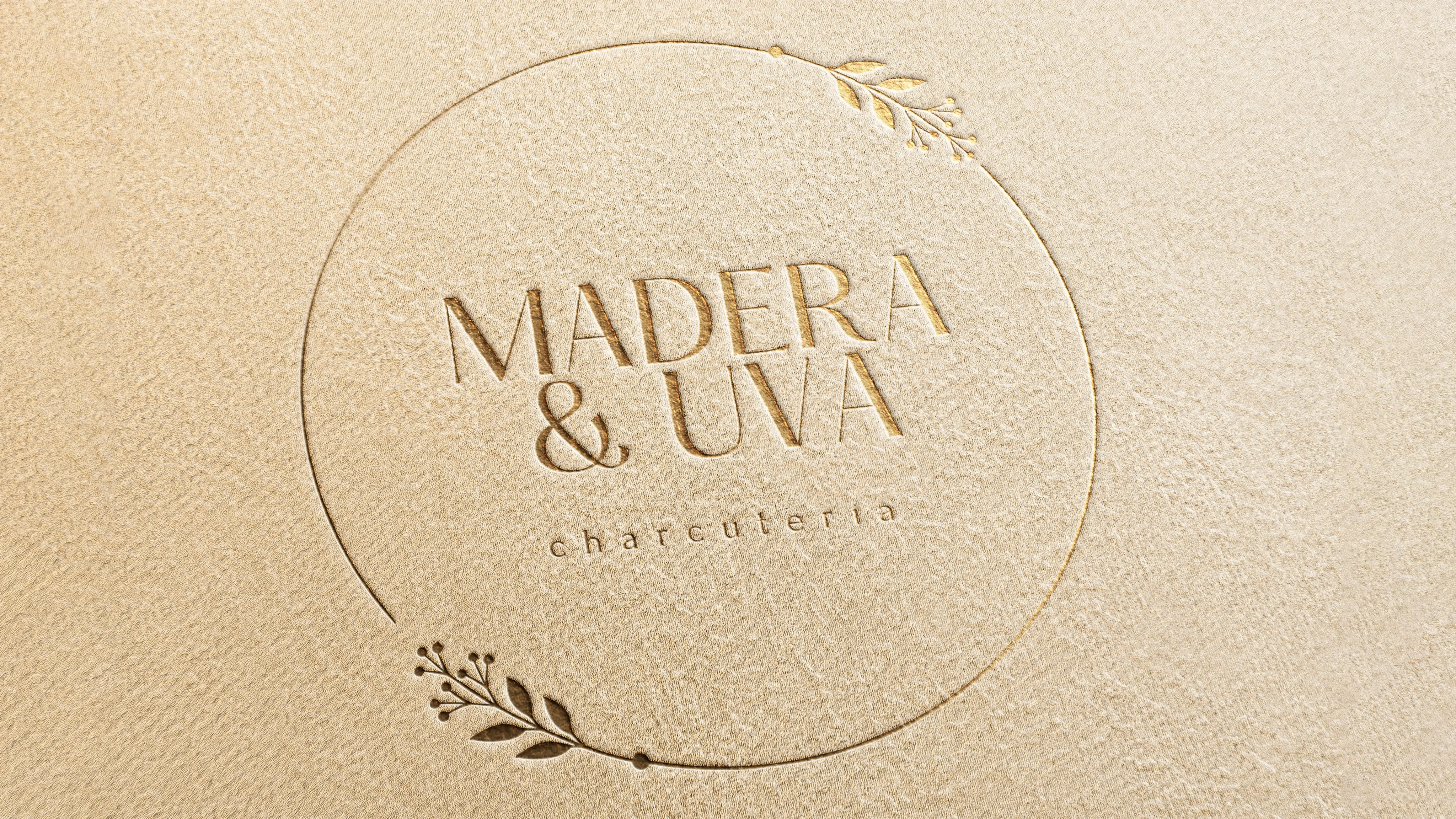Logotipo de "Madera y Uva" en relieve dorado sobre papel texturizado
