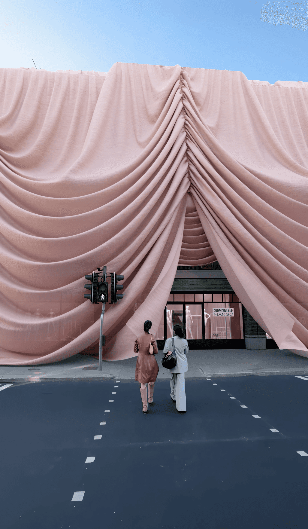 Two women walk toward a Mango storefront draped in massive, flowing pink fabric in mixed reality