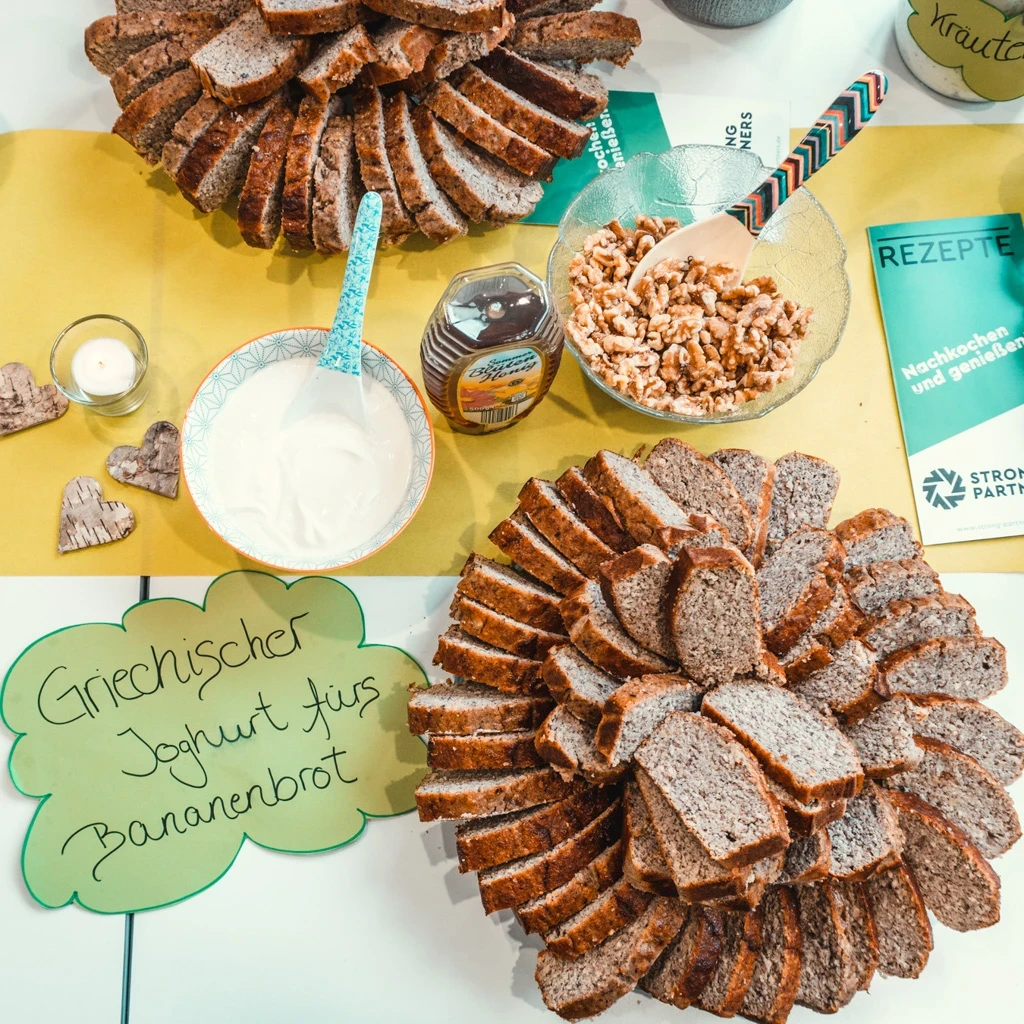 Ein Tisch mit aufgeschnittenem Brot und griechischem Joghurt, daneben liegen Schilder und Flyer von Strong Partners