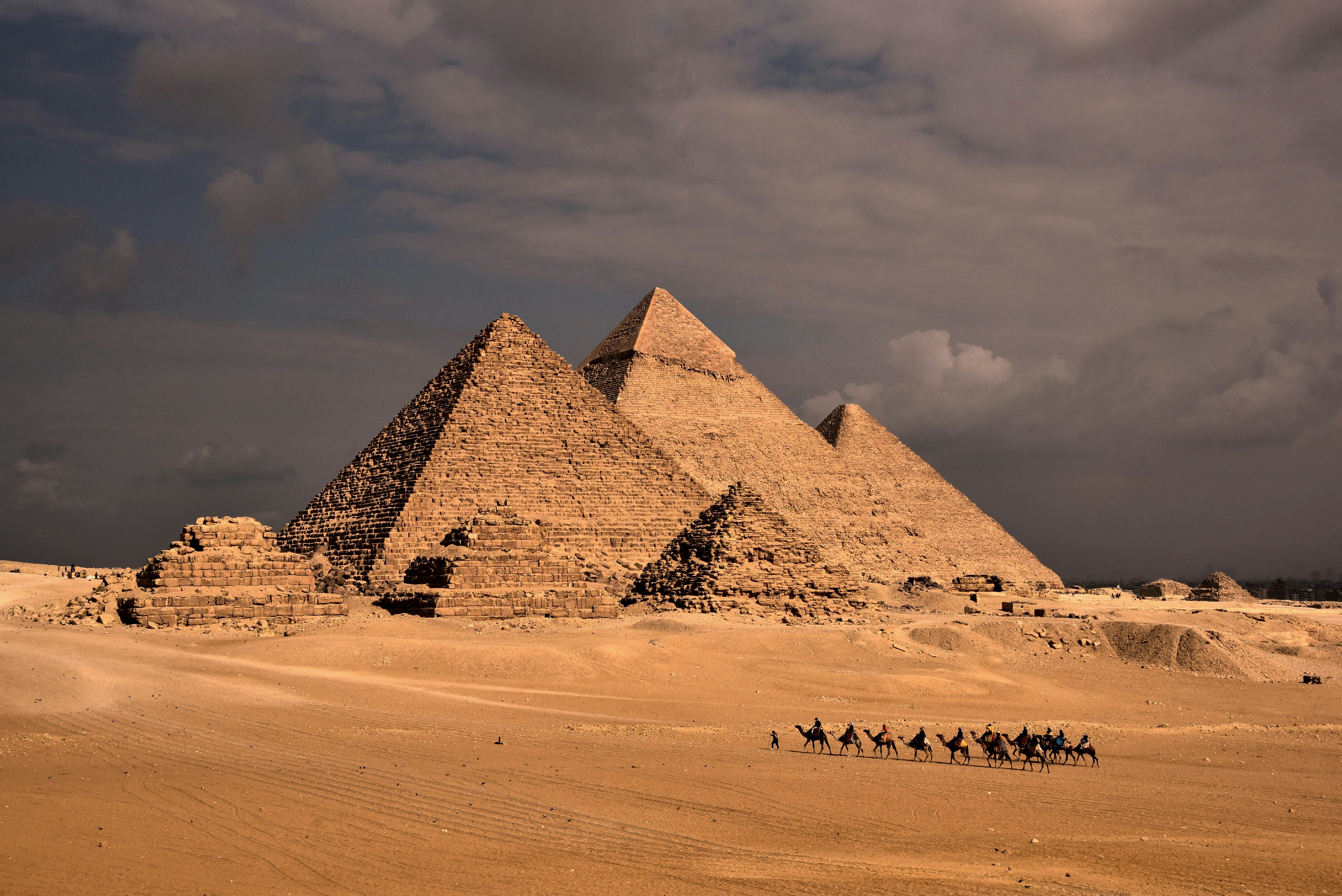 a group of people riding camels in front of three pyramids
