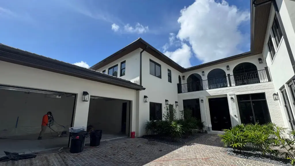 Courtyard of a white Miami home with arched balcony windows, a three car garage, and a paver driveway under construction