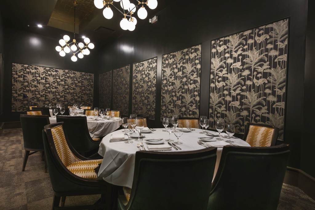 A hand uses a spoon to serve a bowl of creamy pasta with sausage and herbs.