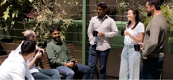 Group of coworkers talking and relaxing together in an outdoor office courtyard during daylight.