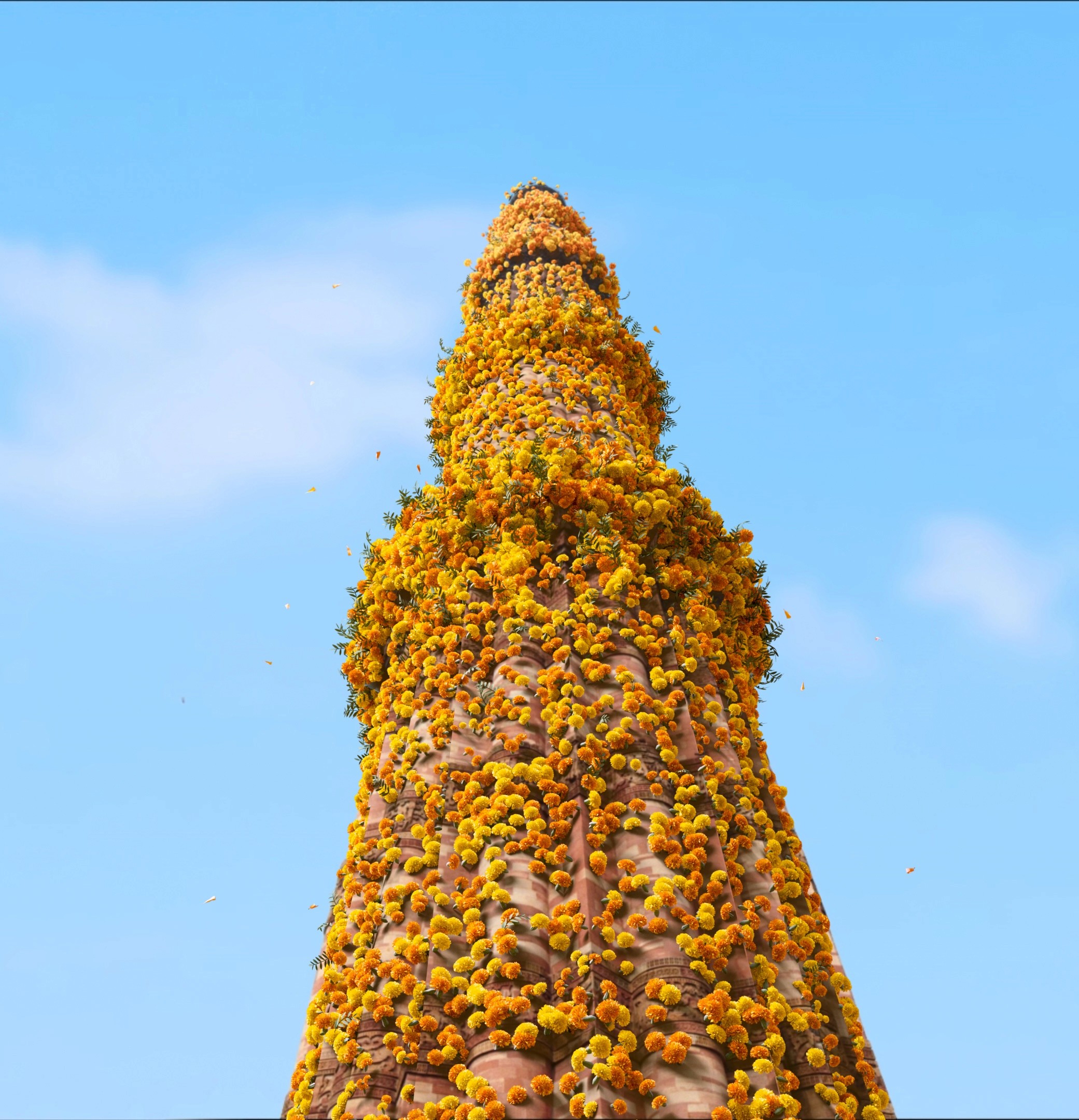 Tall stone tower covered densely with orange marigold flowers against a blue sky