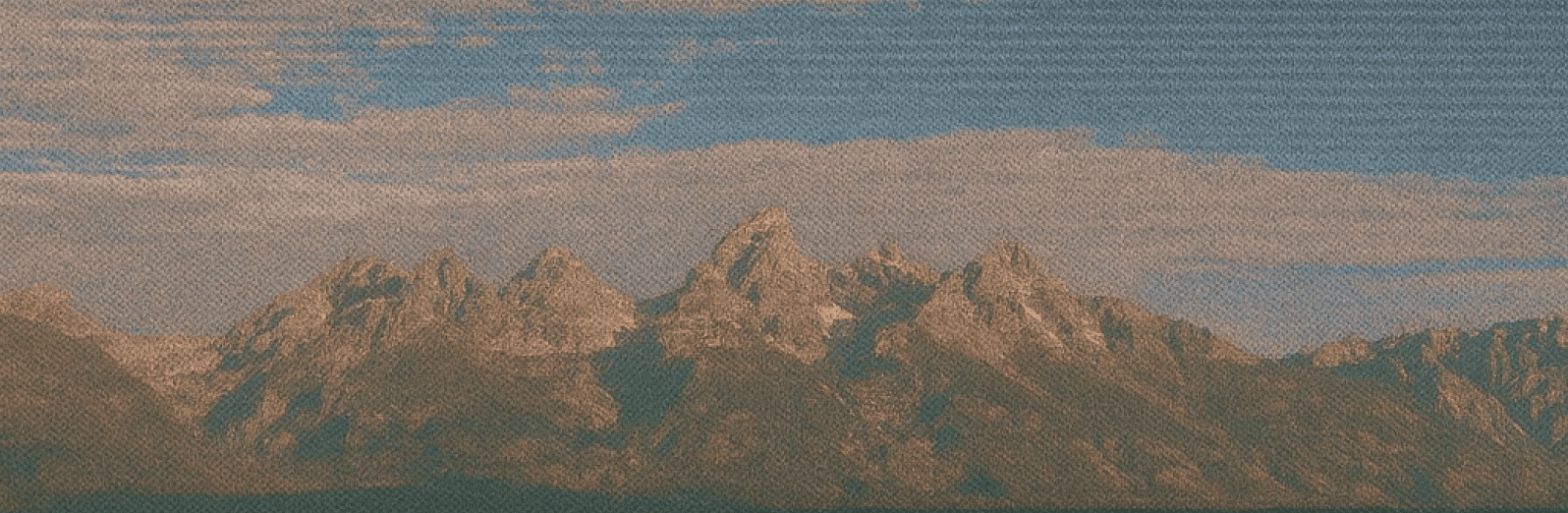 Panoramic view of jagged mountain peaks fading into a muted, cloudy horizon.