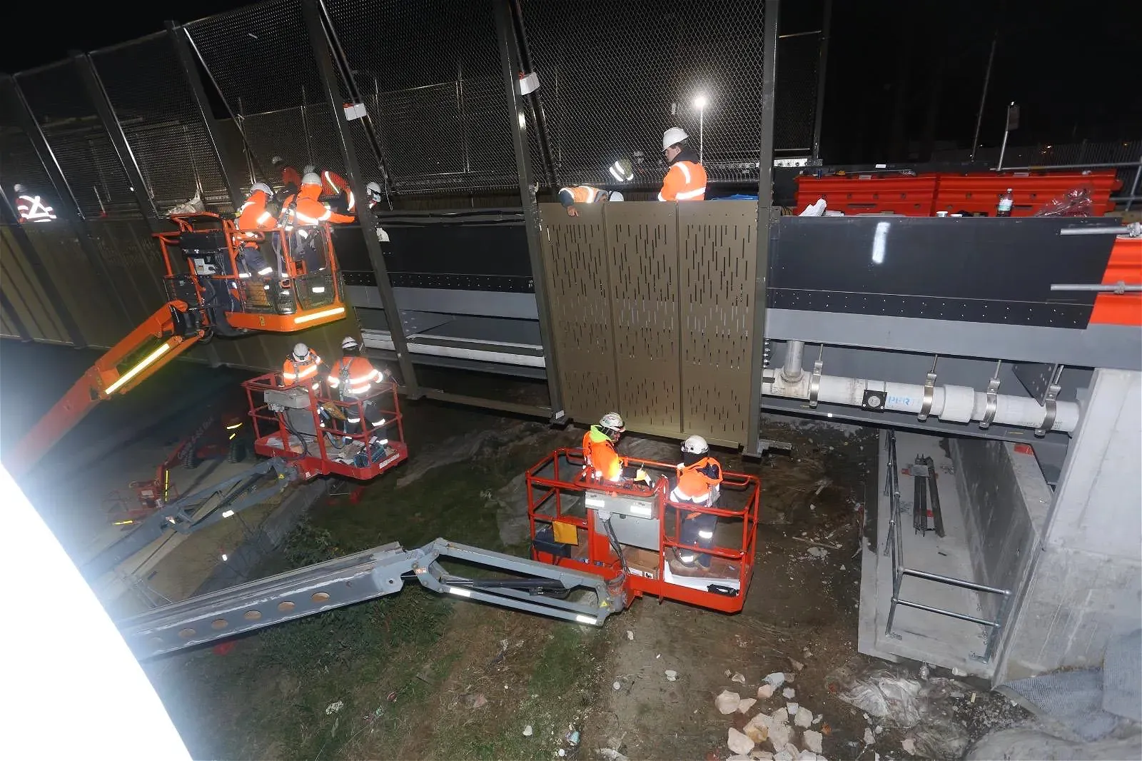 Workers in lifts work on overhead structure at night.