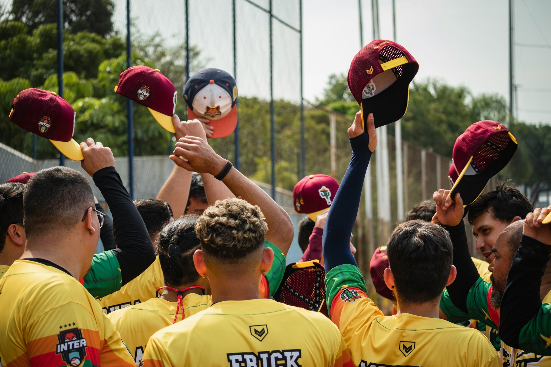 A baseball team in yellow jerseys huddles together, raising their maroon caps in the air.